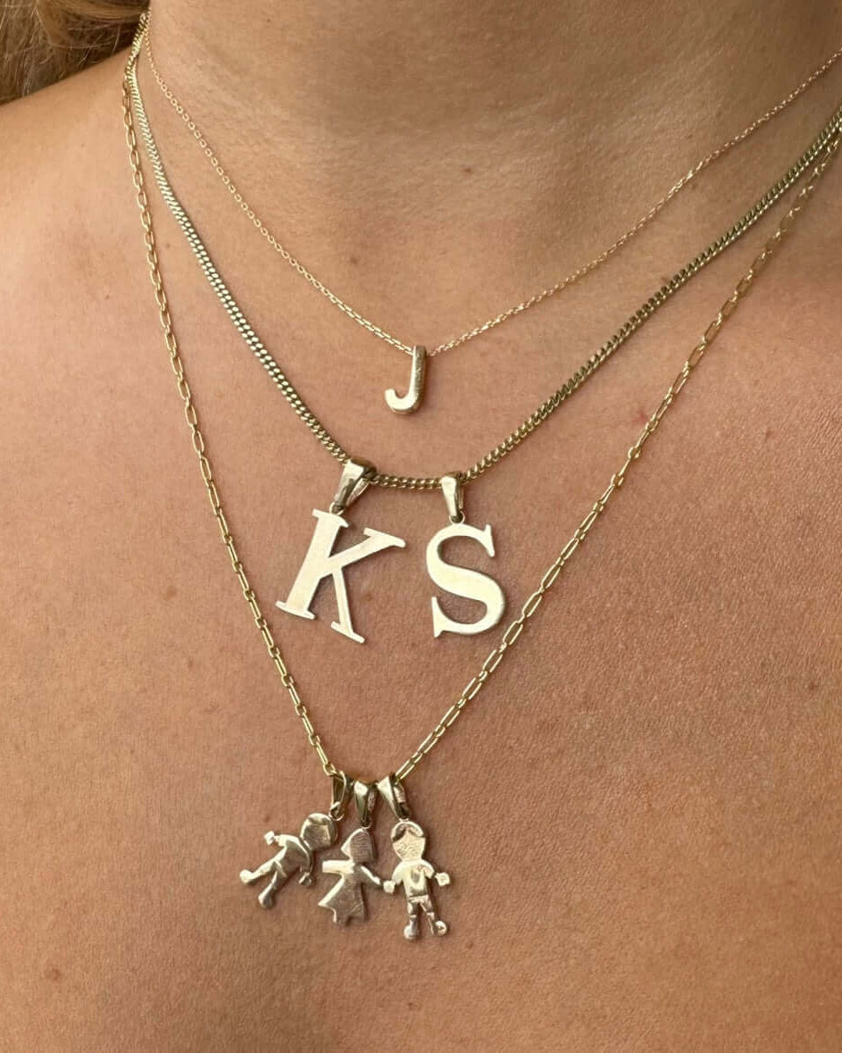 Close-up of layered gold personalized initials jewelry featuring 'J', 'KS', and charm necklaces.