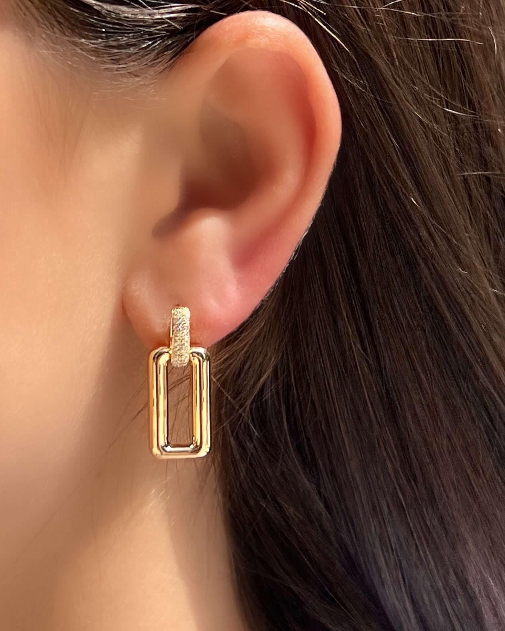 Stylish gold drop earrings featuring a unique geometric design, worn on a model's ear.