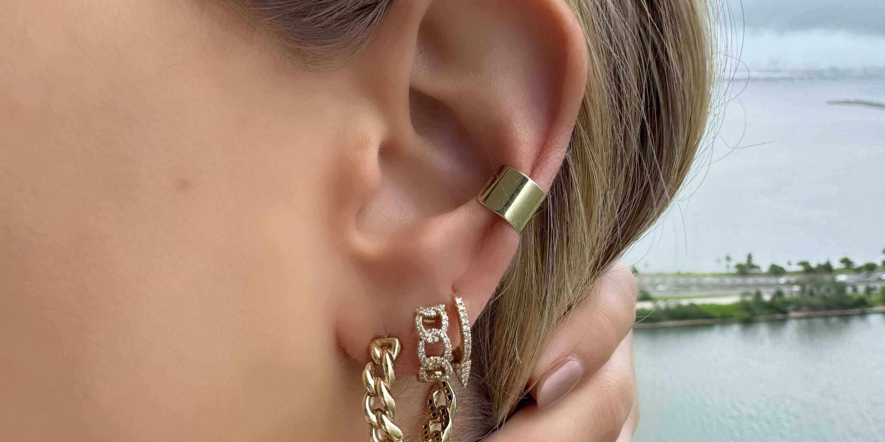 Close-up of a woman wearing stylish gold earrings with a chain design, by a scenic water view.