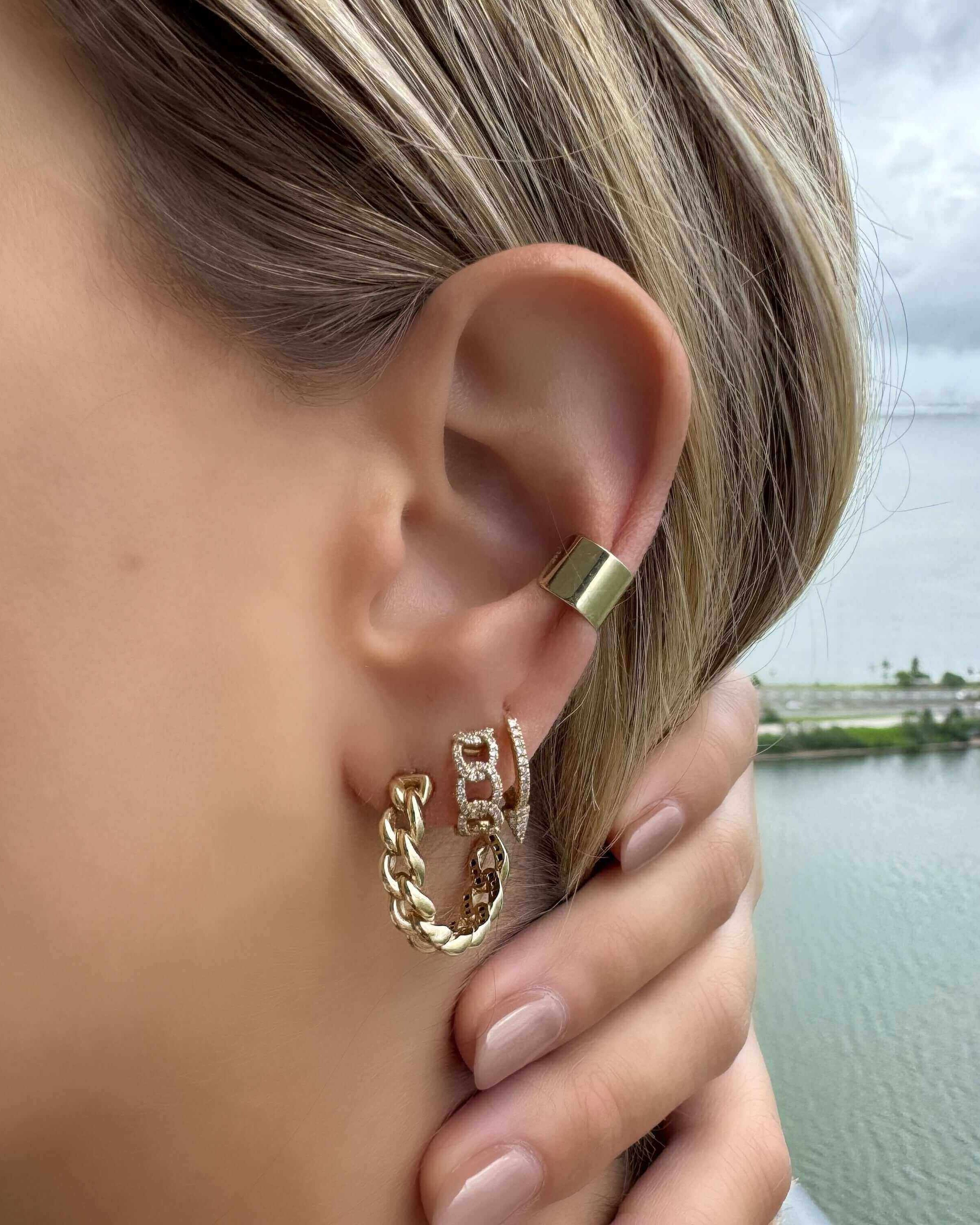 Close-up of a woman wearing stylish gold earrings with a chain design, by a scenic water view.