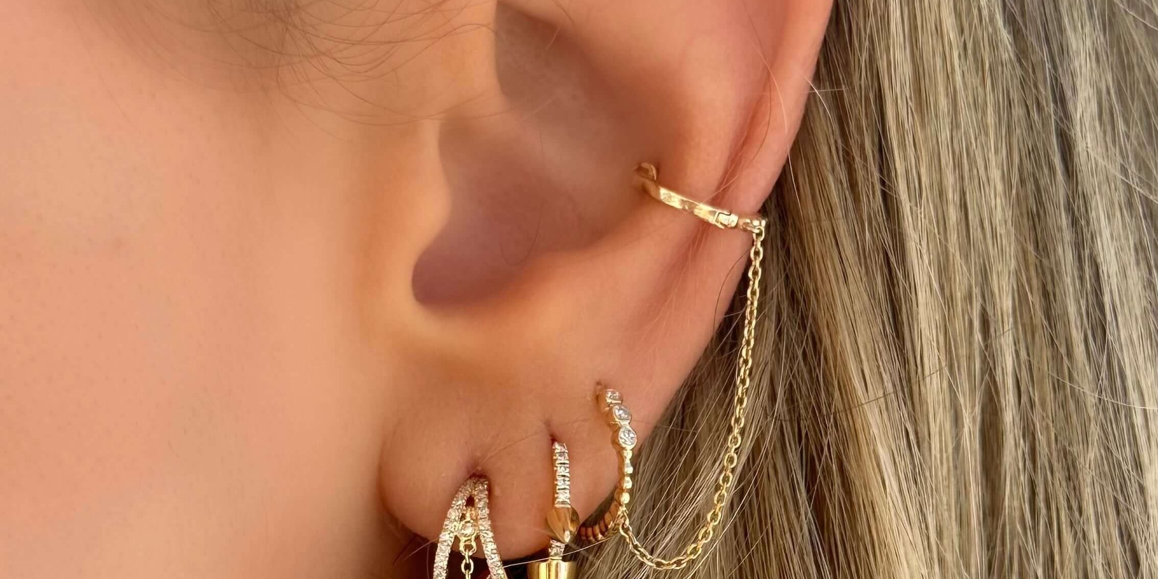 Close-up of intricate gold chained earrings on a woman's ear, featuring sparkling elements and a modern design.