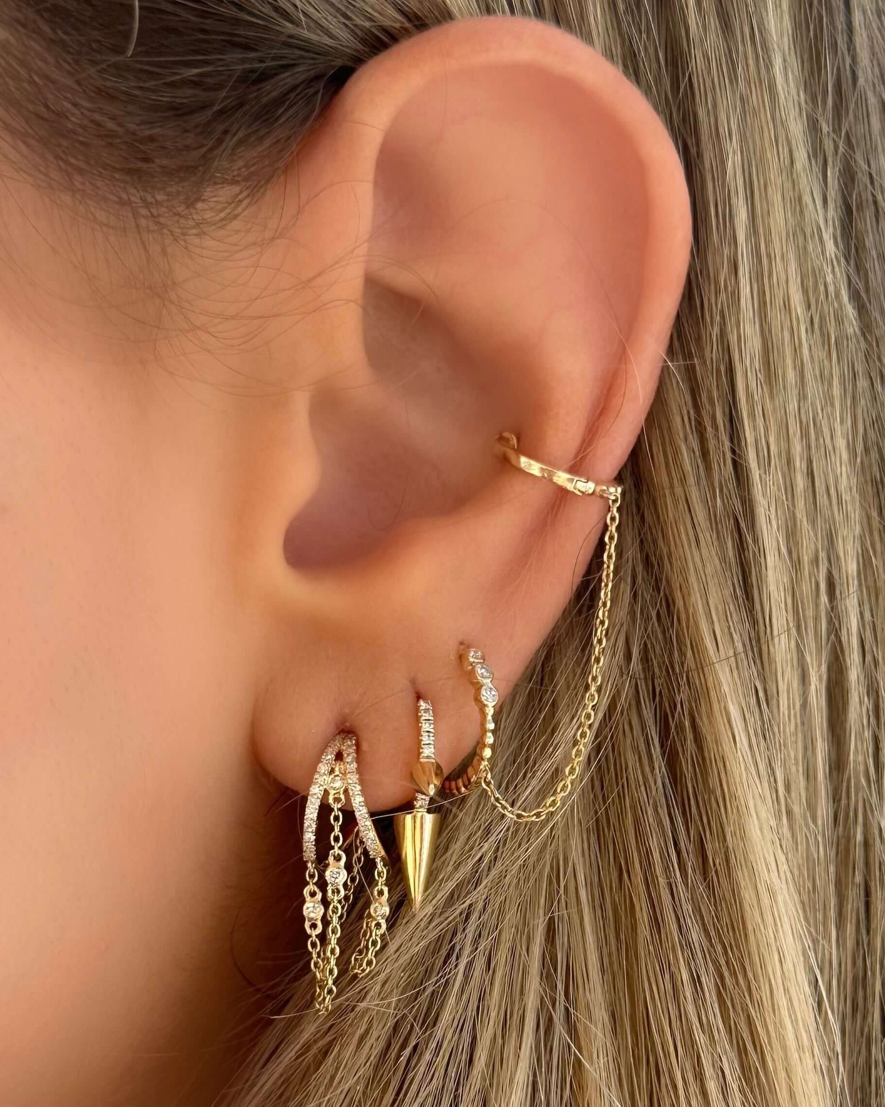 Close-up of intricate gold chained earrings on a woman's ear, featuring sparkling elements and a modern design.