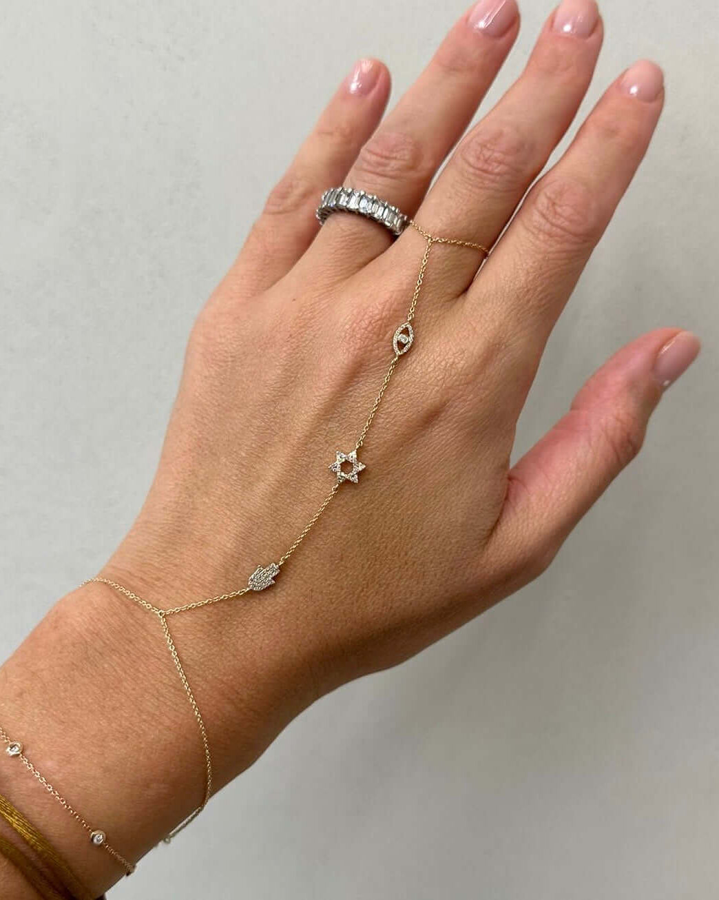 Elegant hand chains featuring a gold design with stars and hamsa charms, adorned on a woman's hand.