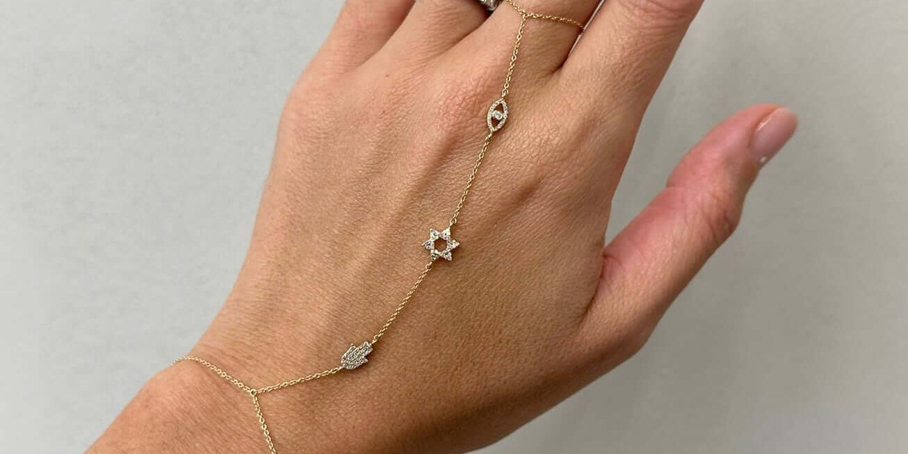 Elegant hand chains featuring a gold design with stars and hamsa charms, adorned on a woman's hand.