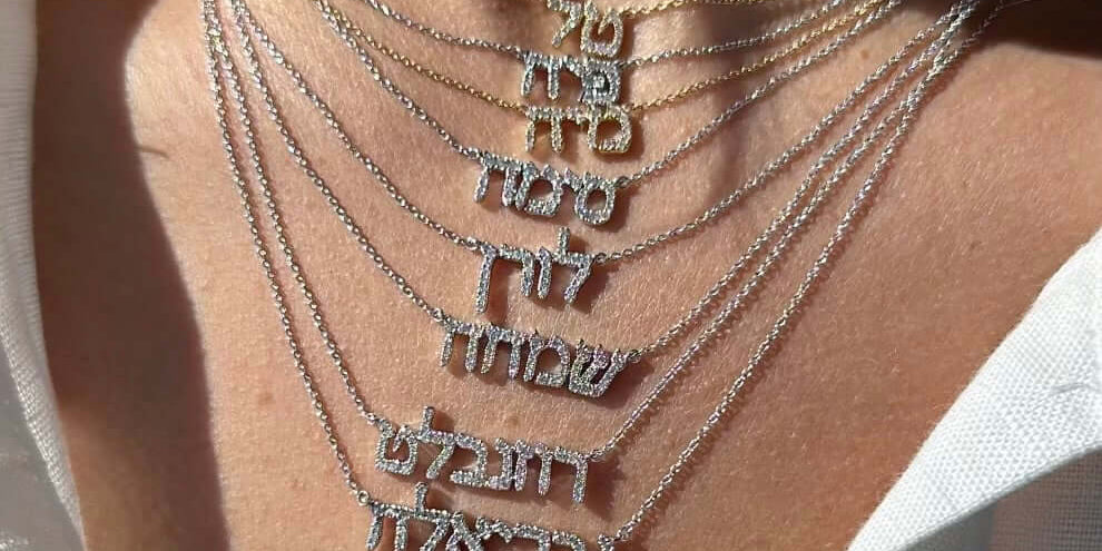 Close-up of layered Hebrew personalized necklaces in gold and silver, showcasing unique name designs.