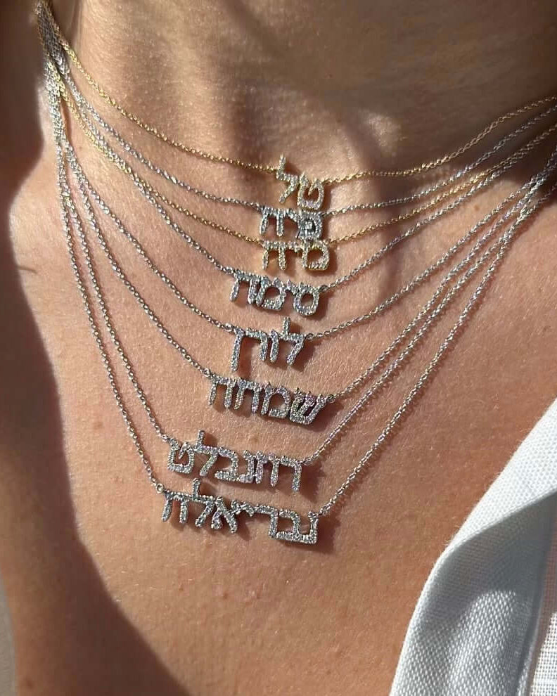 Close-up of layered Hebrew personalized necklaces in gold and silver, showcasing unique name designs.