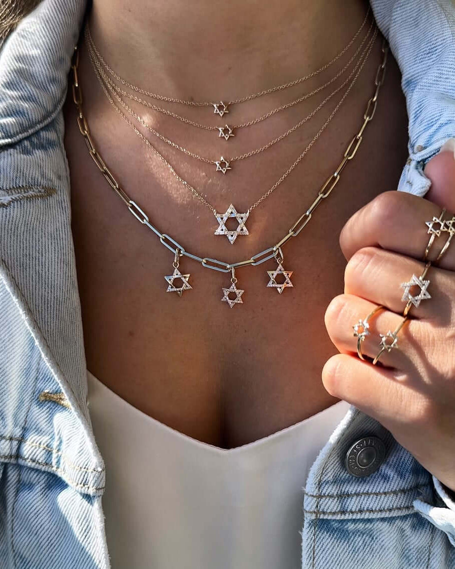 Elegant jewelry featuring multiple Star of David pendants and rings, styled with a denim jacket.