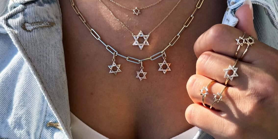 Elegant jewelry featuring multiple Star of David pendants and rings, styled with a denim jacket.