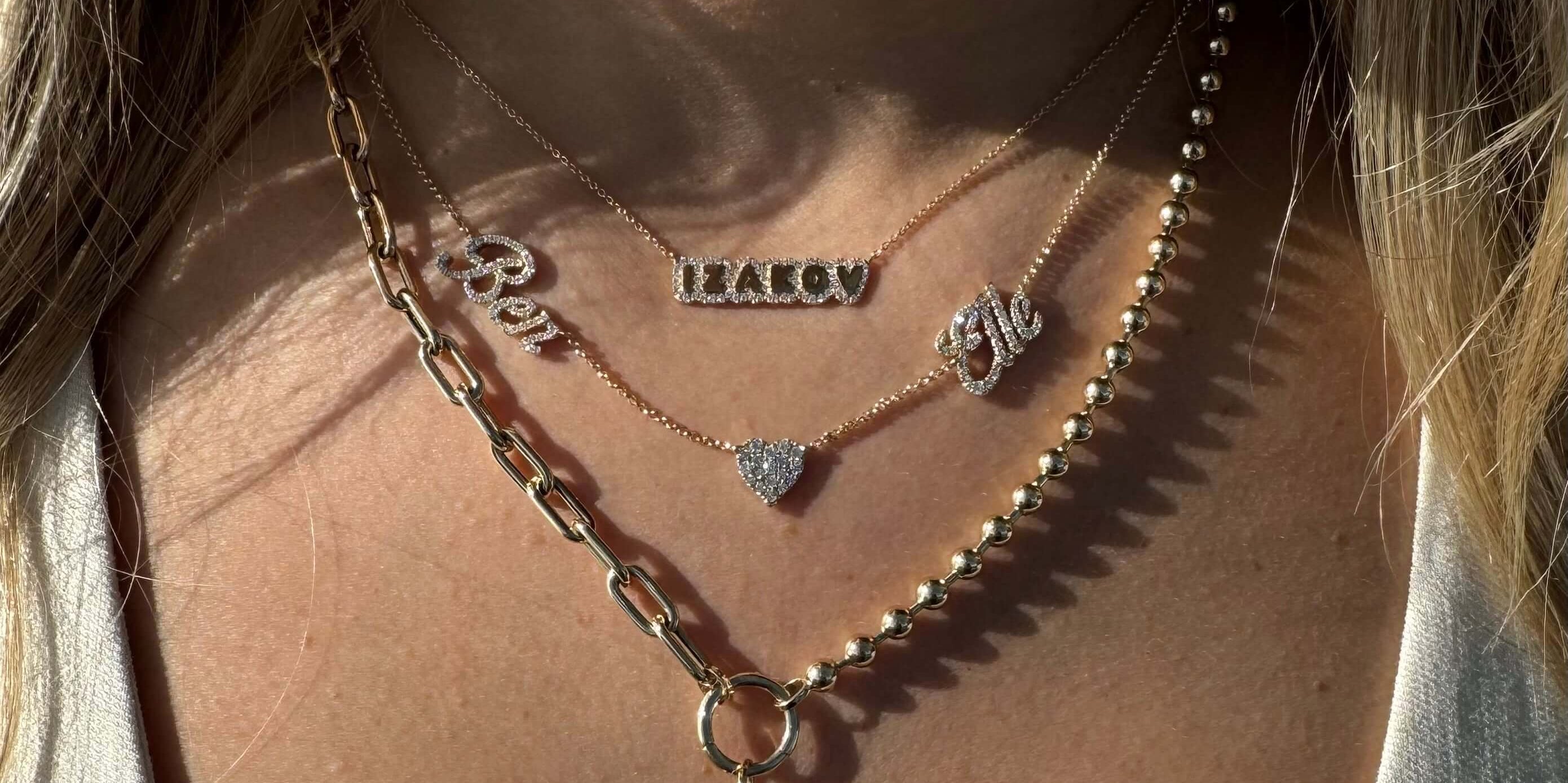 Trendy layered gold necklaces featuring personalized nameplates and a decorative charm, perfect for stylish accessorizing.