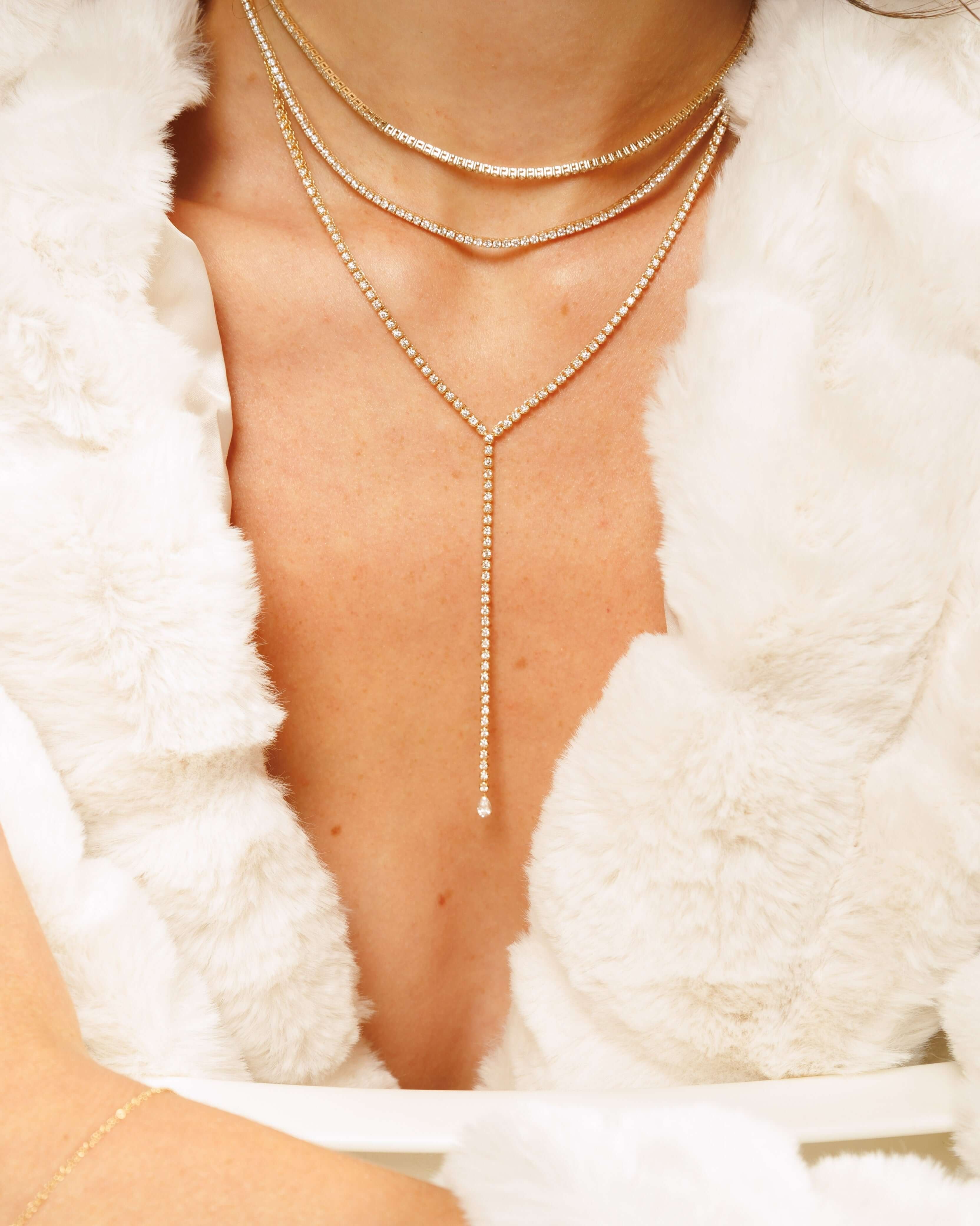 Elegant tennis necklaces layered on a model's neck, showcasing sparkling details against a soft, white fur backdrop.