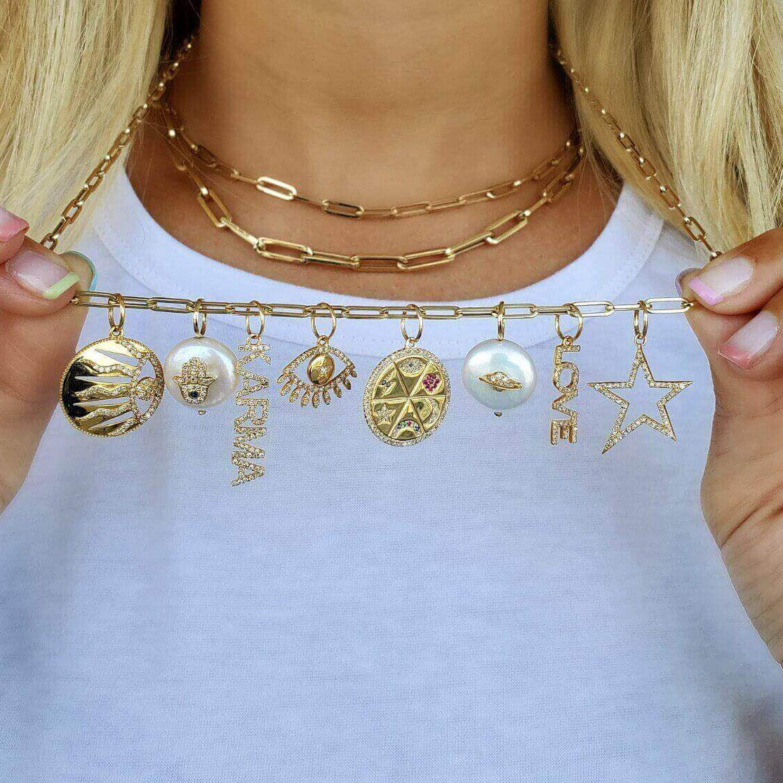 Diamond Accented Hamsa On Flat Pearl Necklace Charm among various gold charms on a chain.
