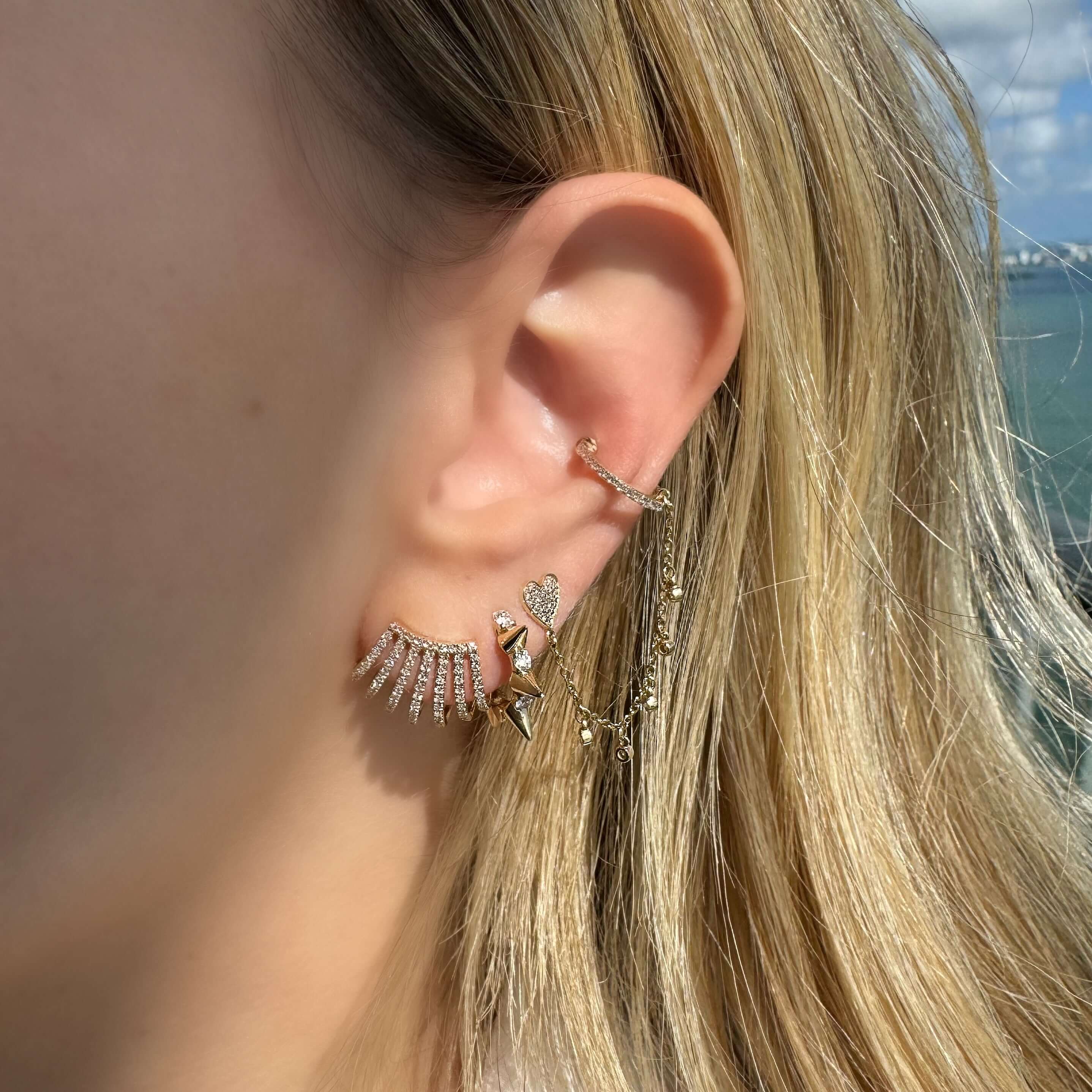 Close-up of a woman's ear adorned with sparkling gold huggie earrings and unique spike designs, showcasing modern earring trends.