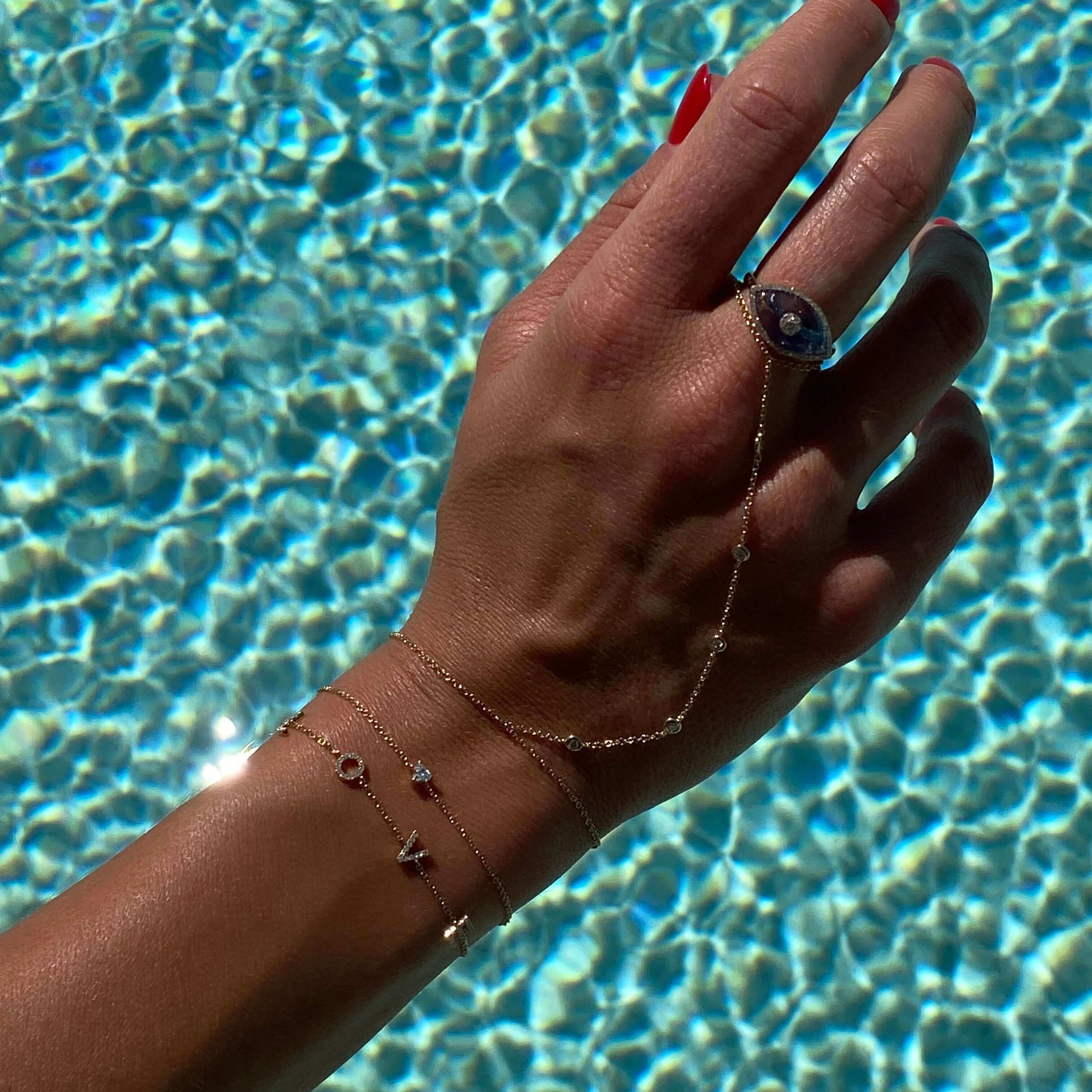 Elegant wrist adorned with delicate jewelry bracelets and a stunning ring, captured against a sparkling pool background.