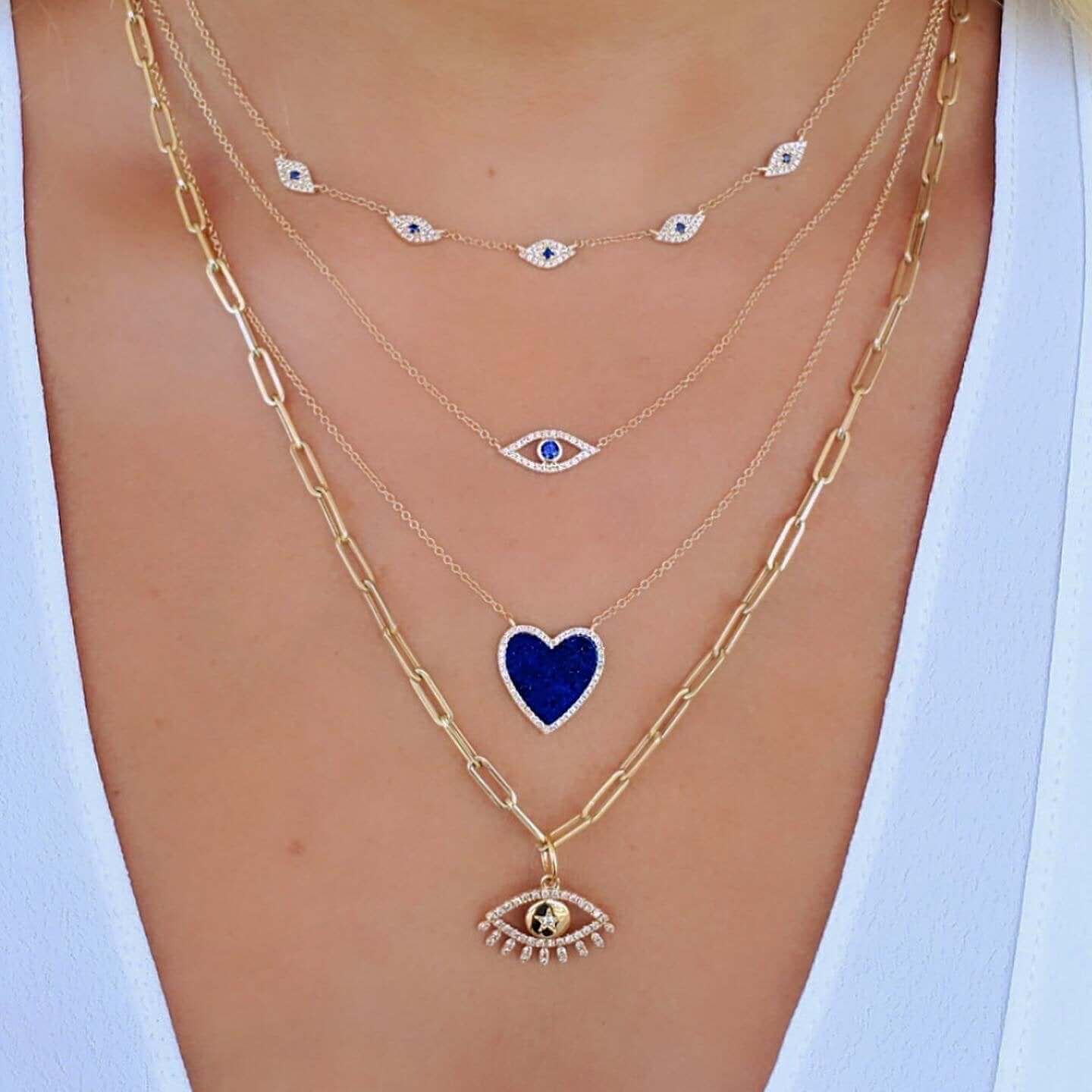 Woman wearing layered gold necklaces with heart and evil eye pendants, showcasing delicate jewelry from our brand.