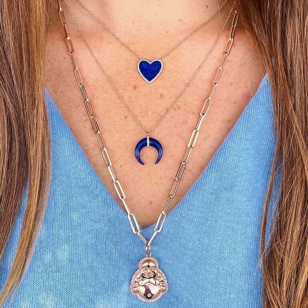 Woman wearing layered necklaces with heart, moon, and ornate pendant in gold and blue, from our exclusive jewelry collection