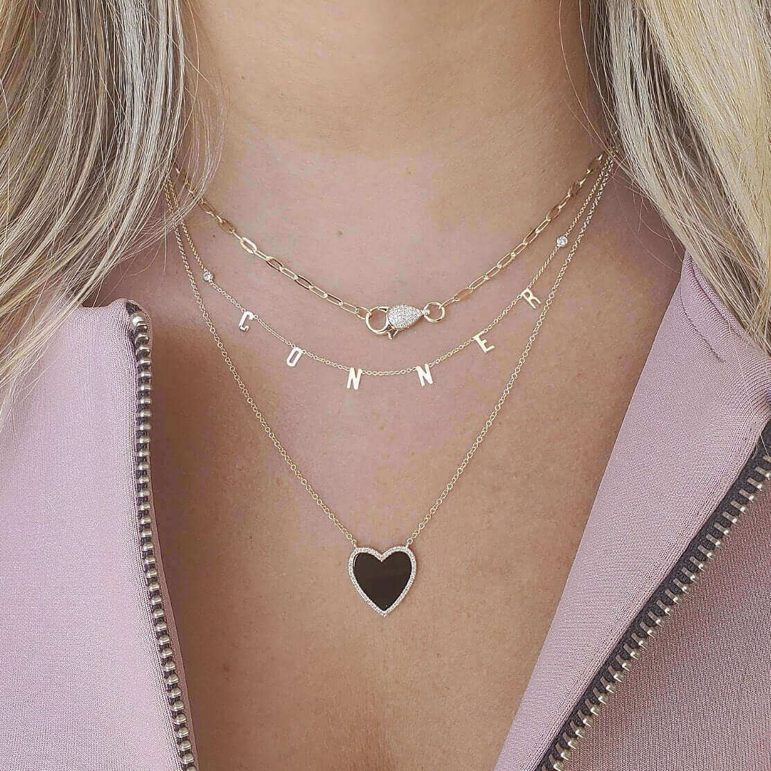 Woman wearing layered gold necklaces with custom name letters and a heart pendant by our jewelry brand.