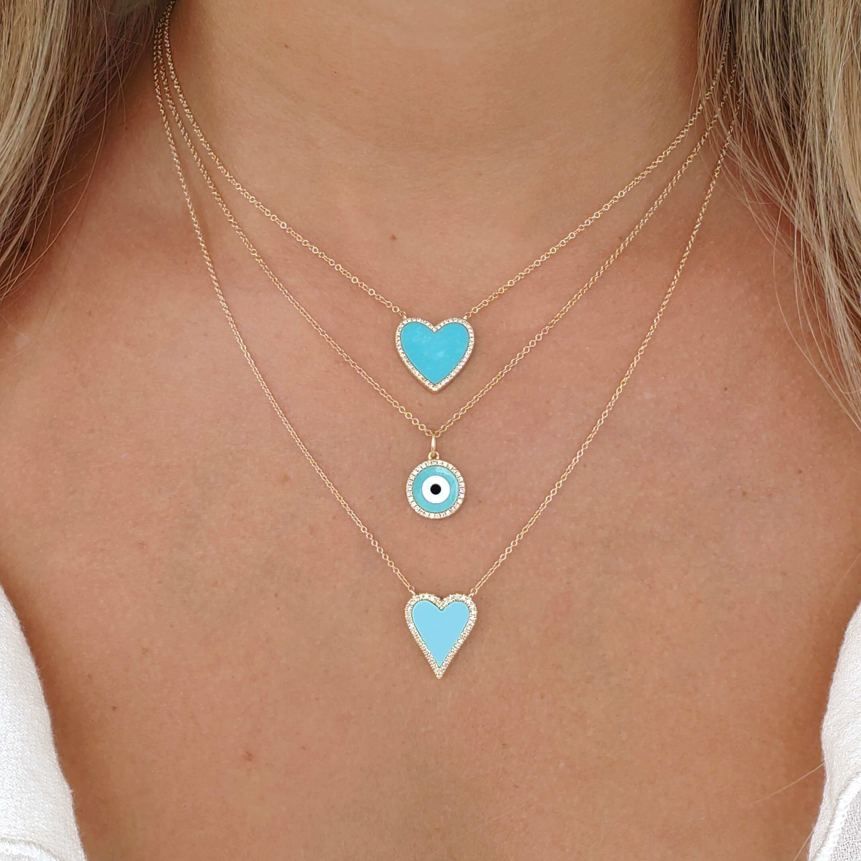 Woman wearing layered turquoise heart and evil eye pendant necklaces from our jewelry brand.