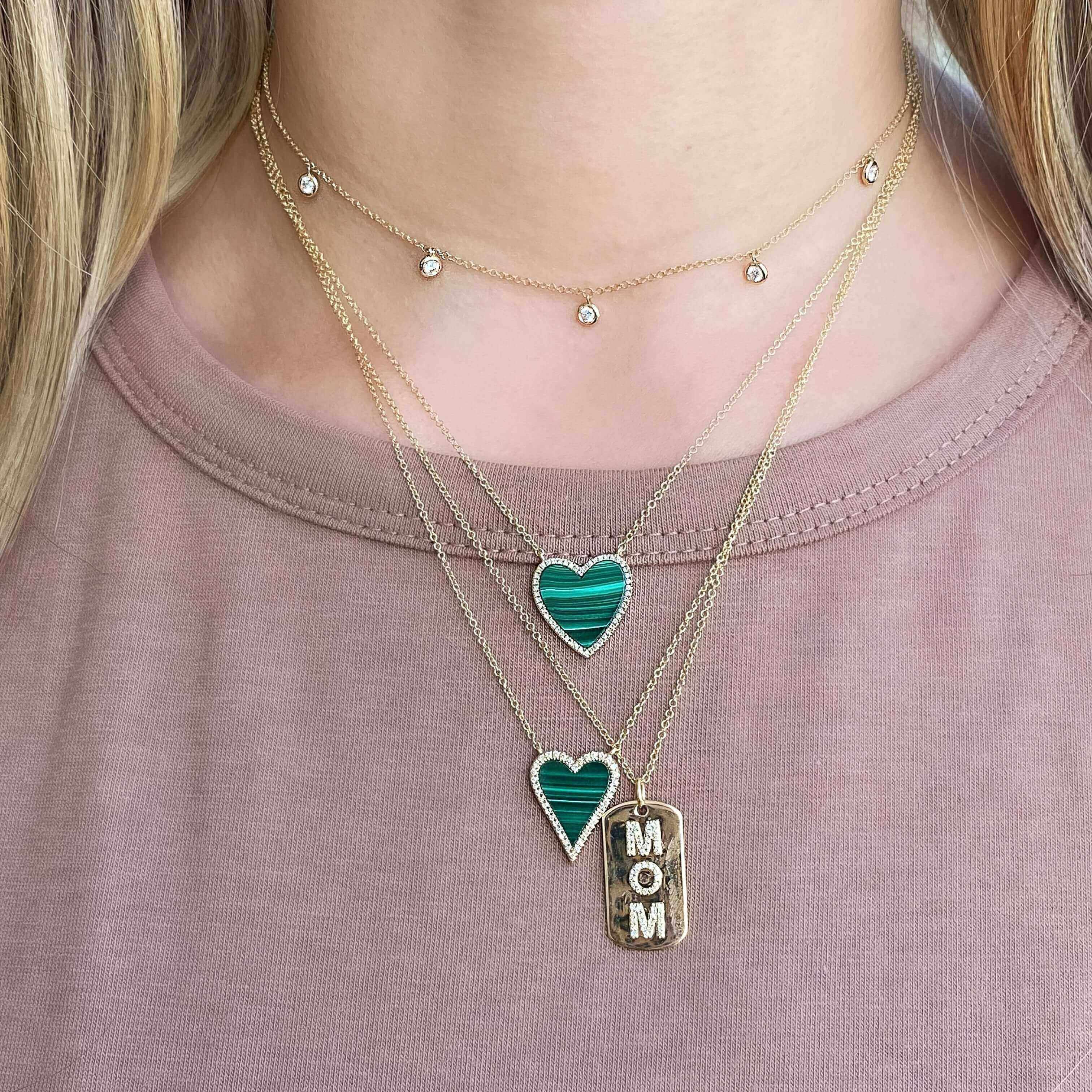Woman wearing layered gold necklaces with heart-shaped and "MOM" pendants from our jewelry collection