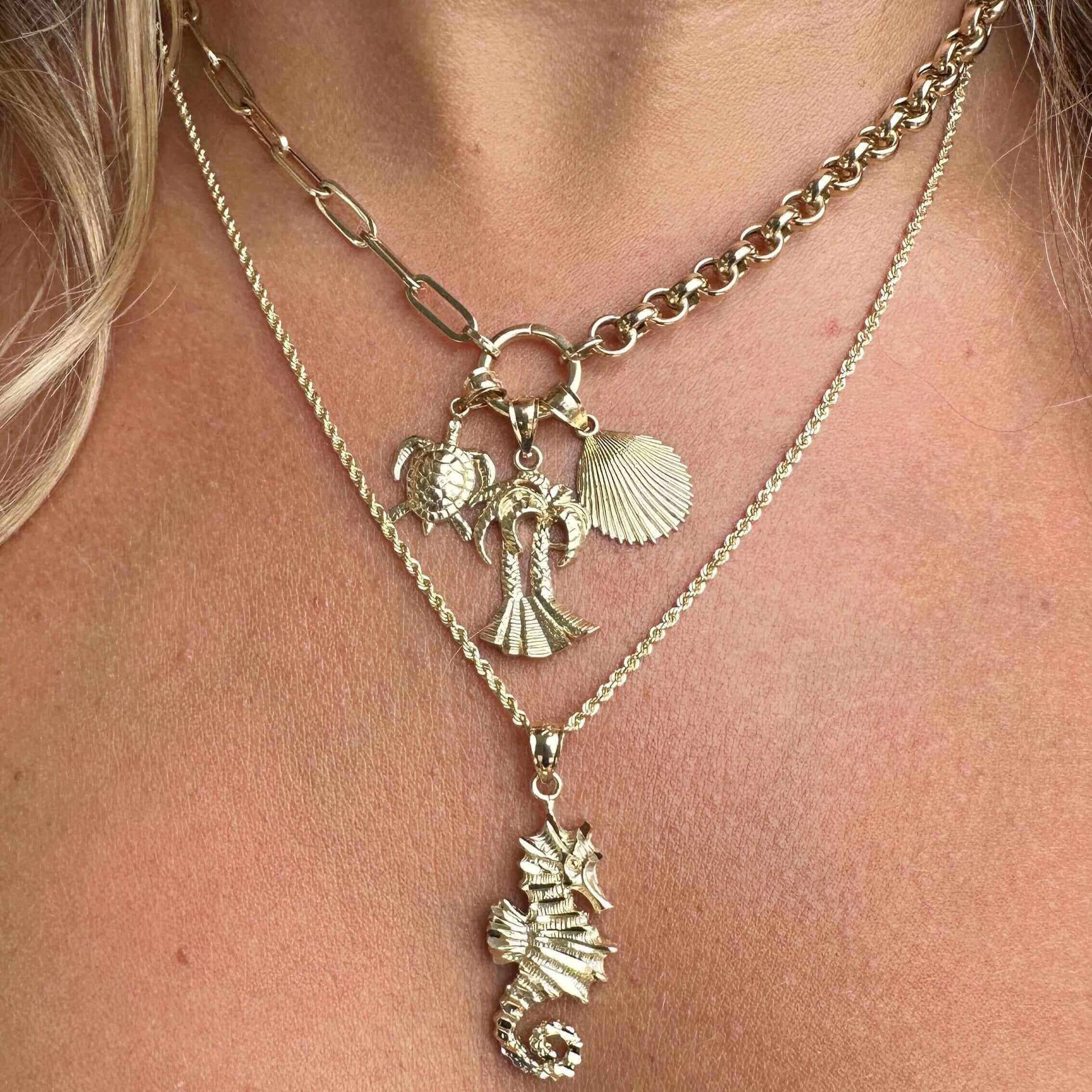 Layered gold necklaces with sea-themed charms featuring a turtle, palm tree, seashell, and seahorse.