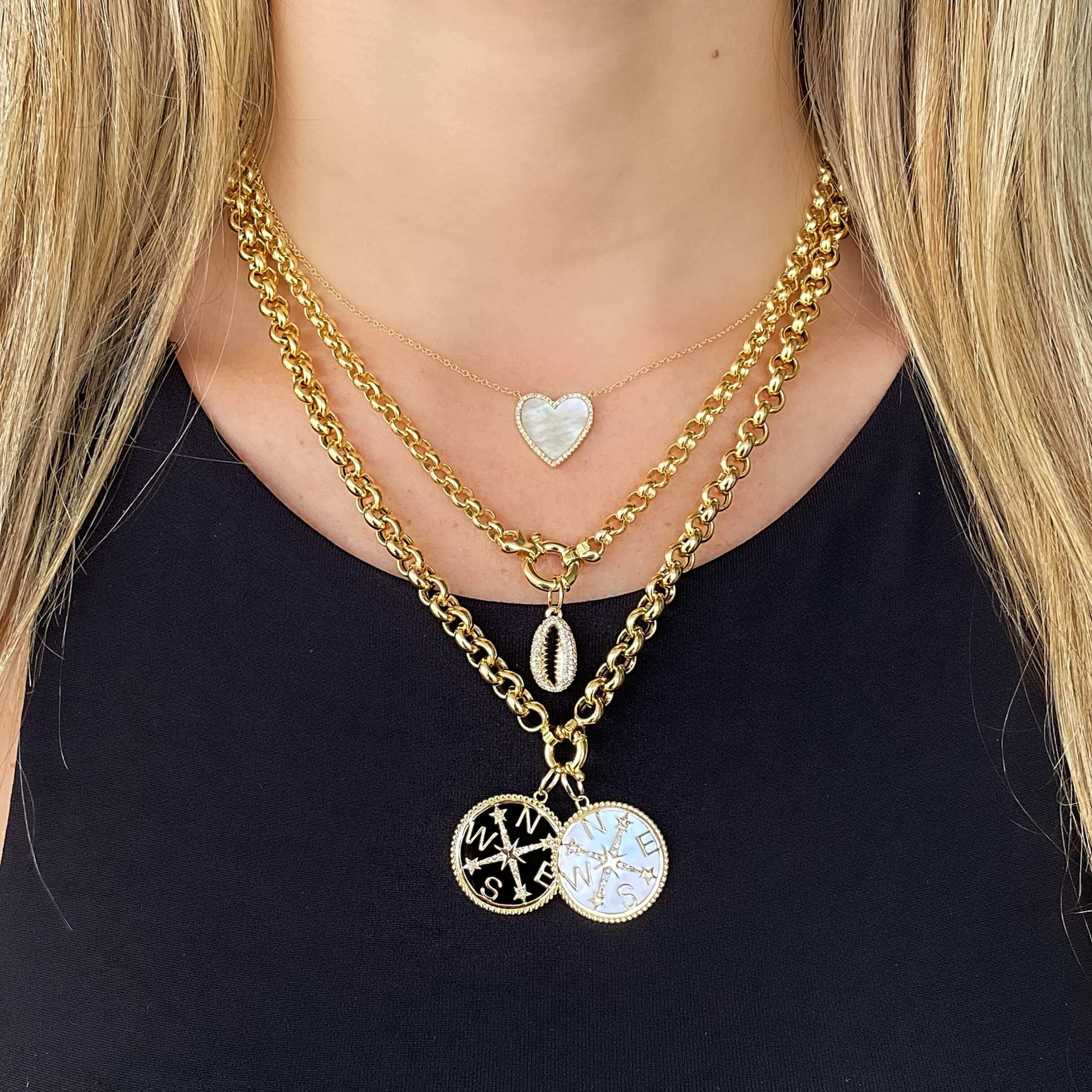 Woman wearing layered gold necklaces with heart, shell, and compass charms from our jewelry brand.