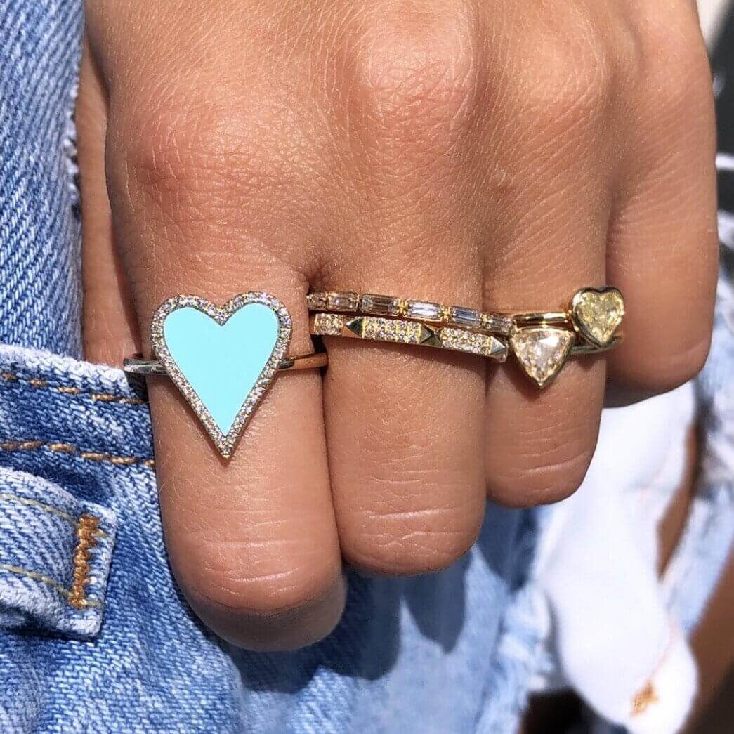 Hand wearing turquoise heart ring, diamond eternity band, and gold heart ring, showcasing trendy jewelry by our brand.