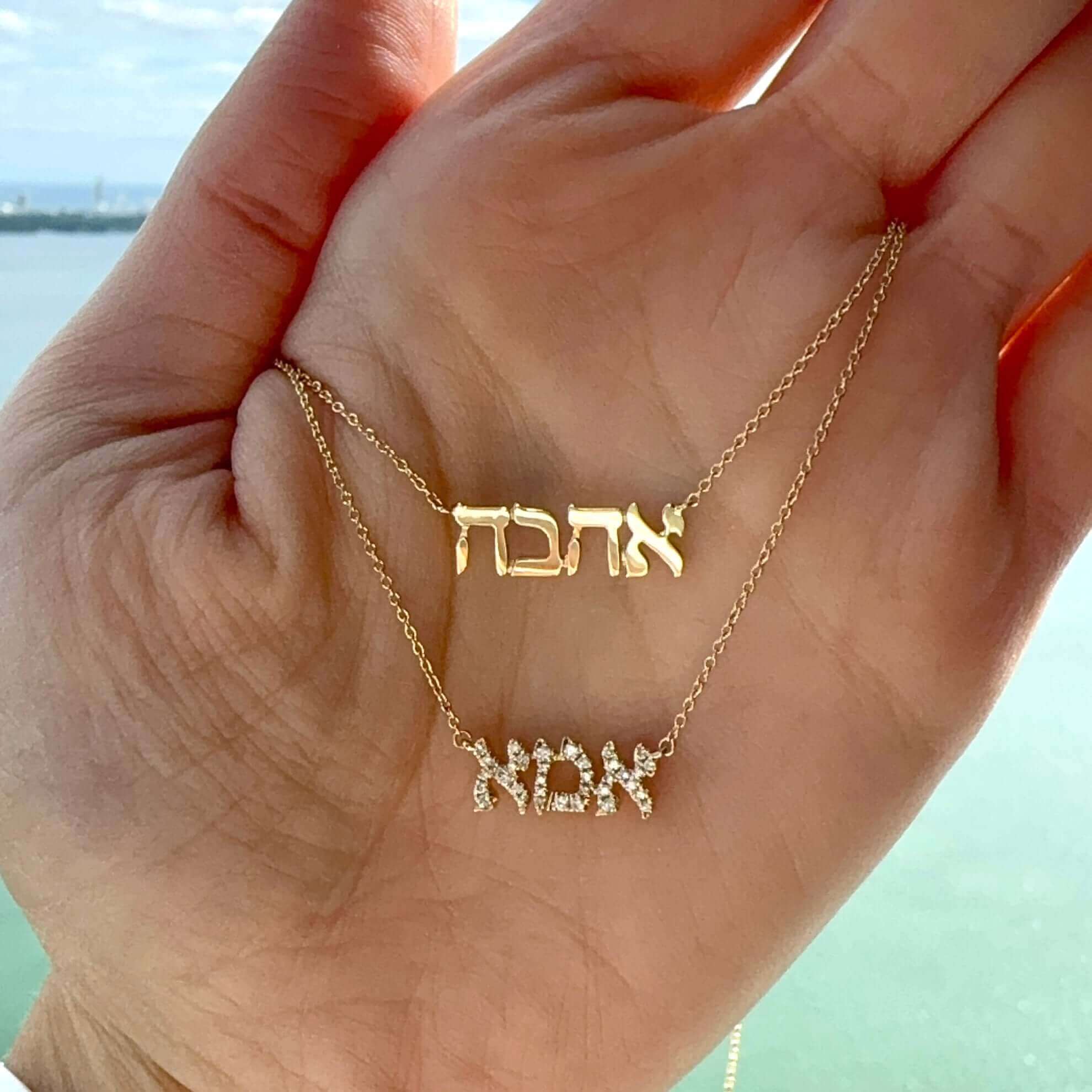 Gold and diamond Hebrew name necklaces from our exclusive jewelry collection displayed on an open palm