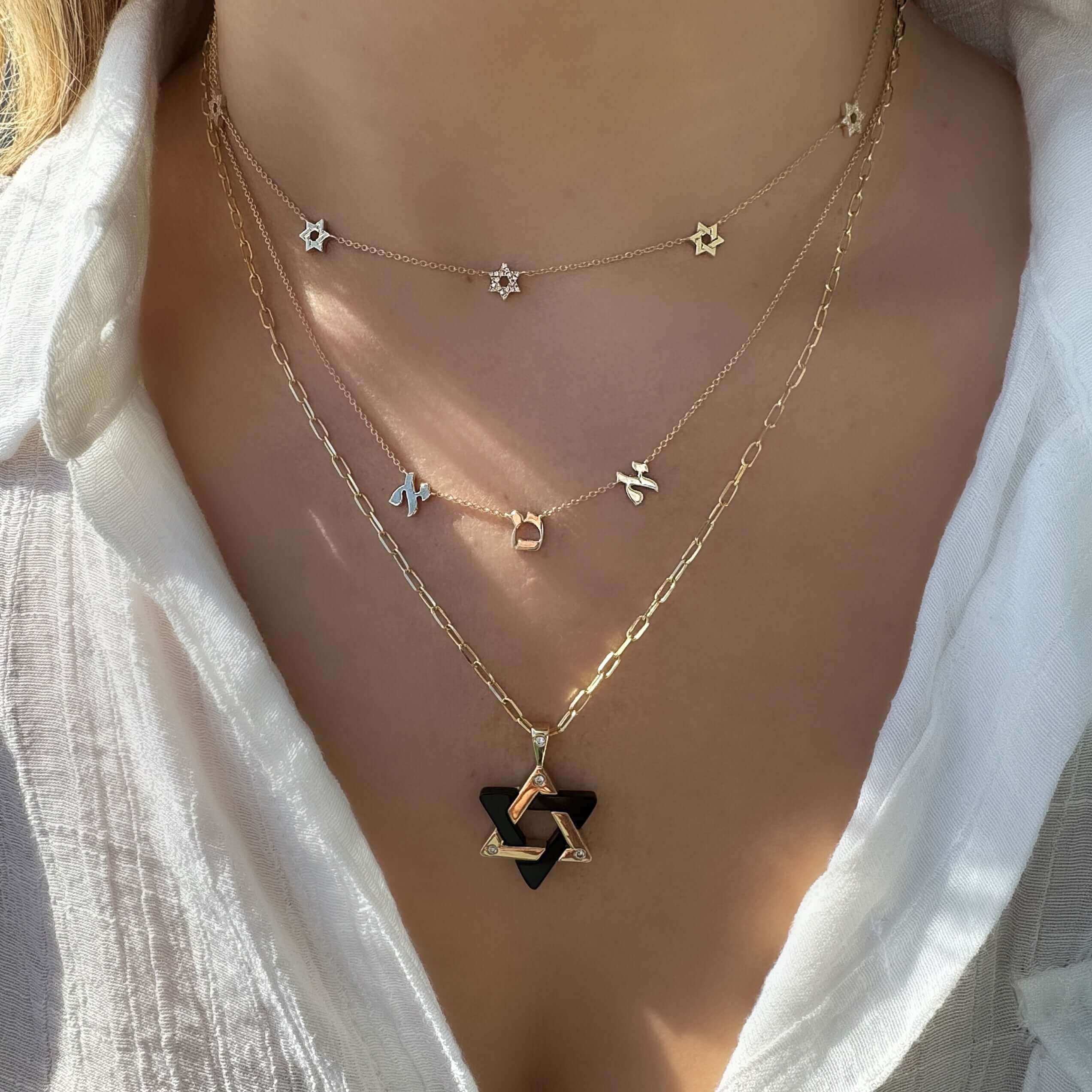 Woman wearing layered gold necklaces with Star of David and Hebrew letter pendants from our jewelry brand.