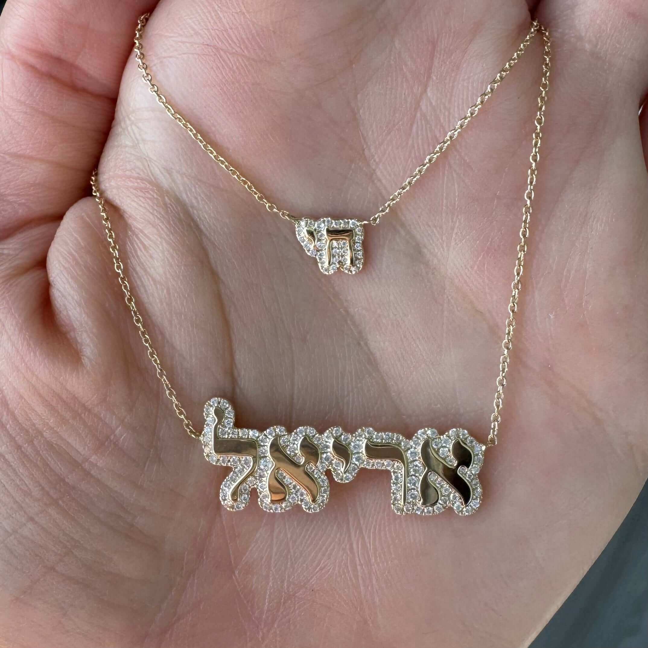 Hand displaying two gold necklaces with Hebrew inscriptions, designed by our luxury jewelry brand.