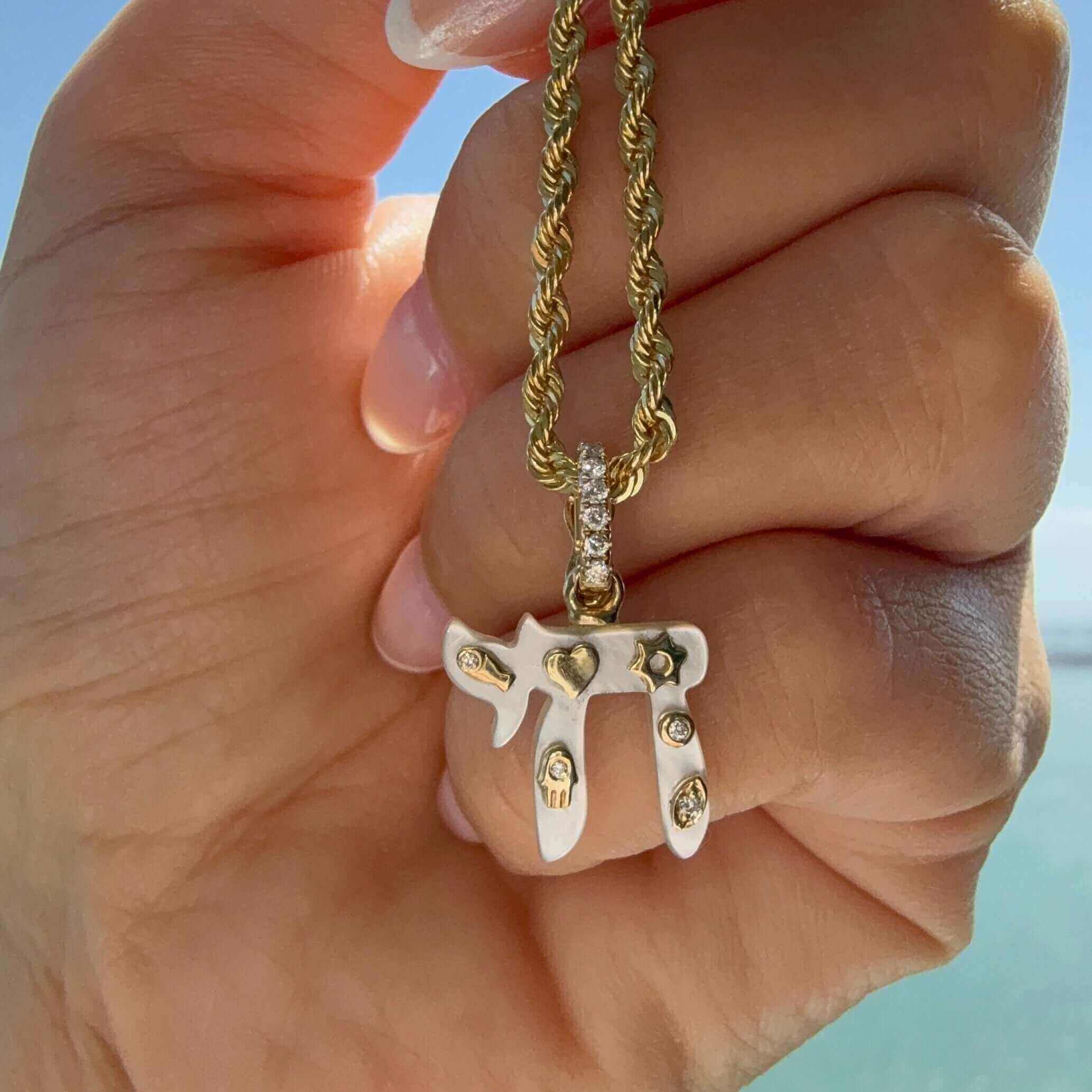 Hand holding a 14K Gold Chai Gemstone Pendant with diamond accents, set against a serene background.
