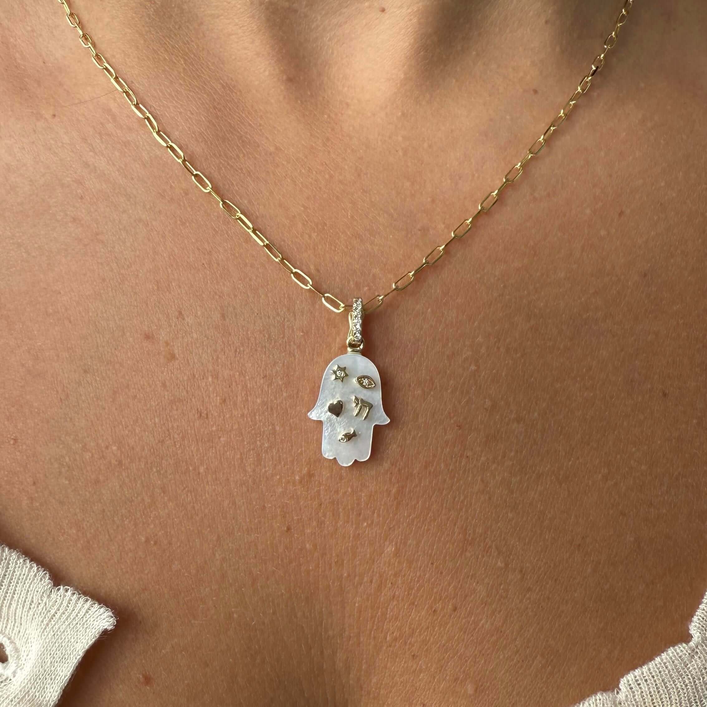 14K gold Hamsa pendant with mother of pearl and diamond accents, worn by a model.