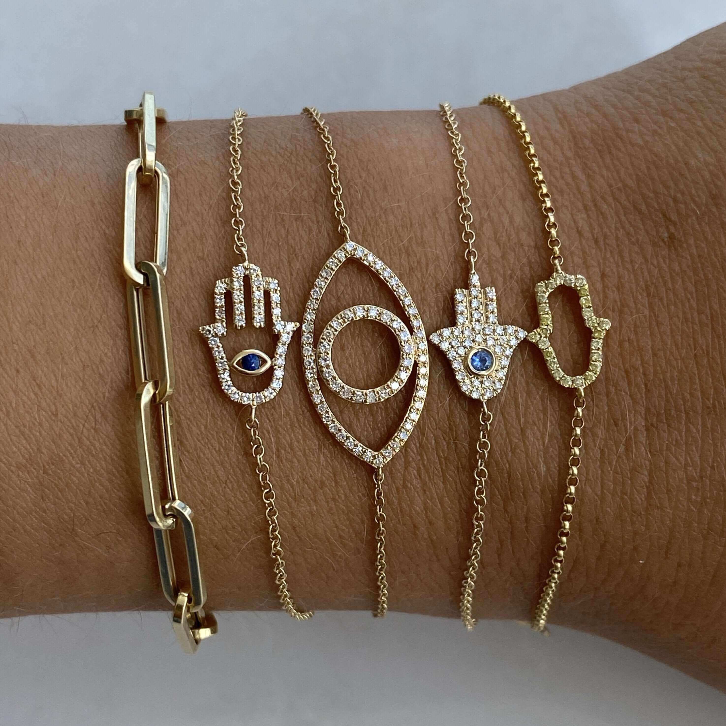 Gold chain and Hamsa hand bracelets featuring blue gemstones from our luxury jewelry collection.