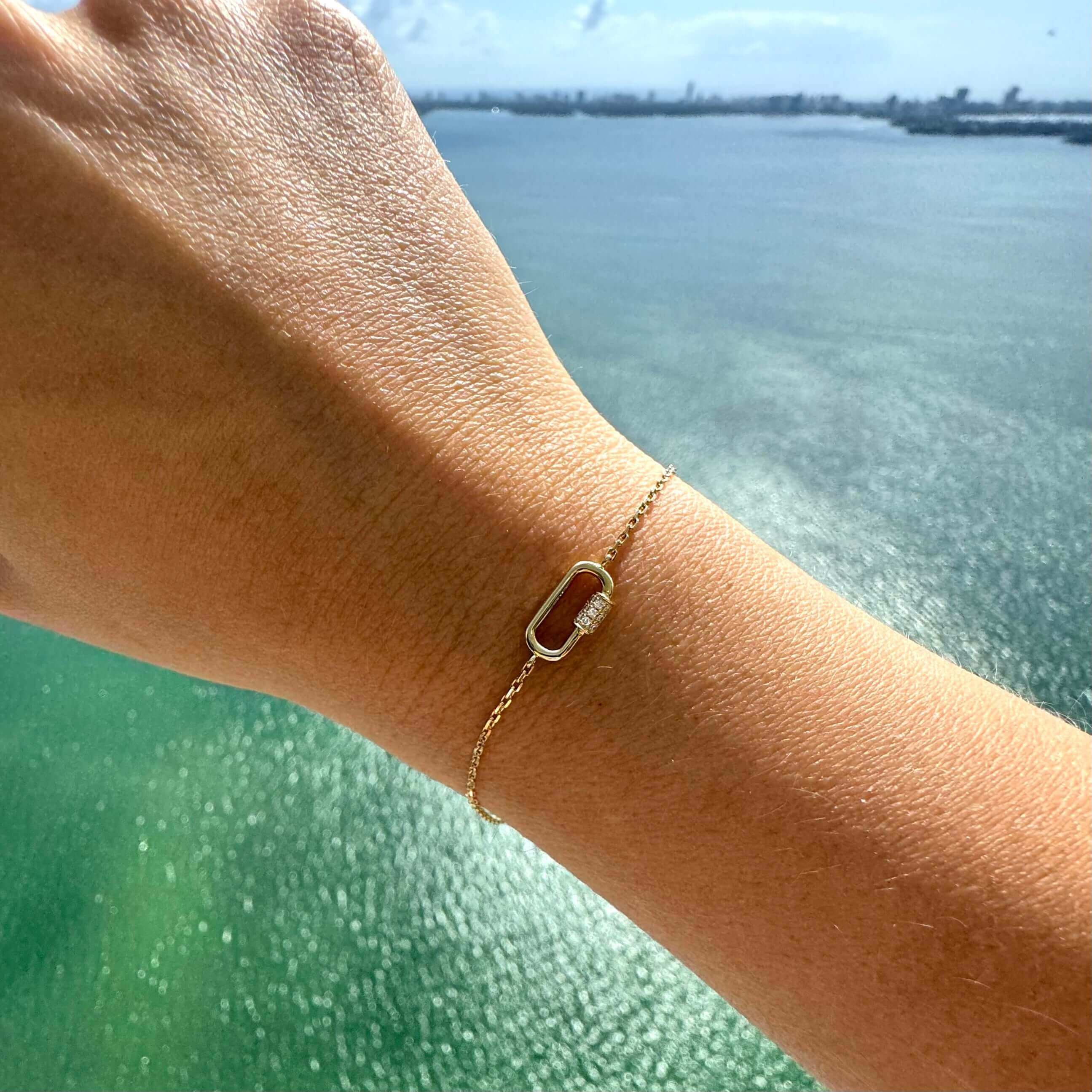 Gold chain bracelet with elegant chain link design on wrist with ocean view in the background from our jewelry brand.