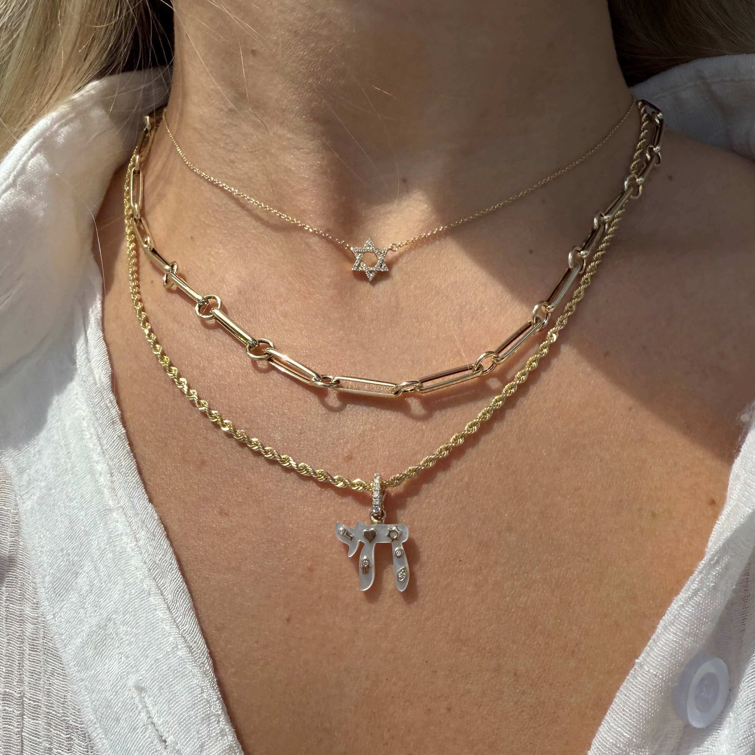 Layered gold necklaces featuring a Chai pendant and a Star of David charm on a woman.