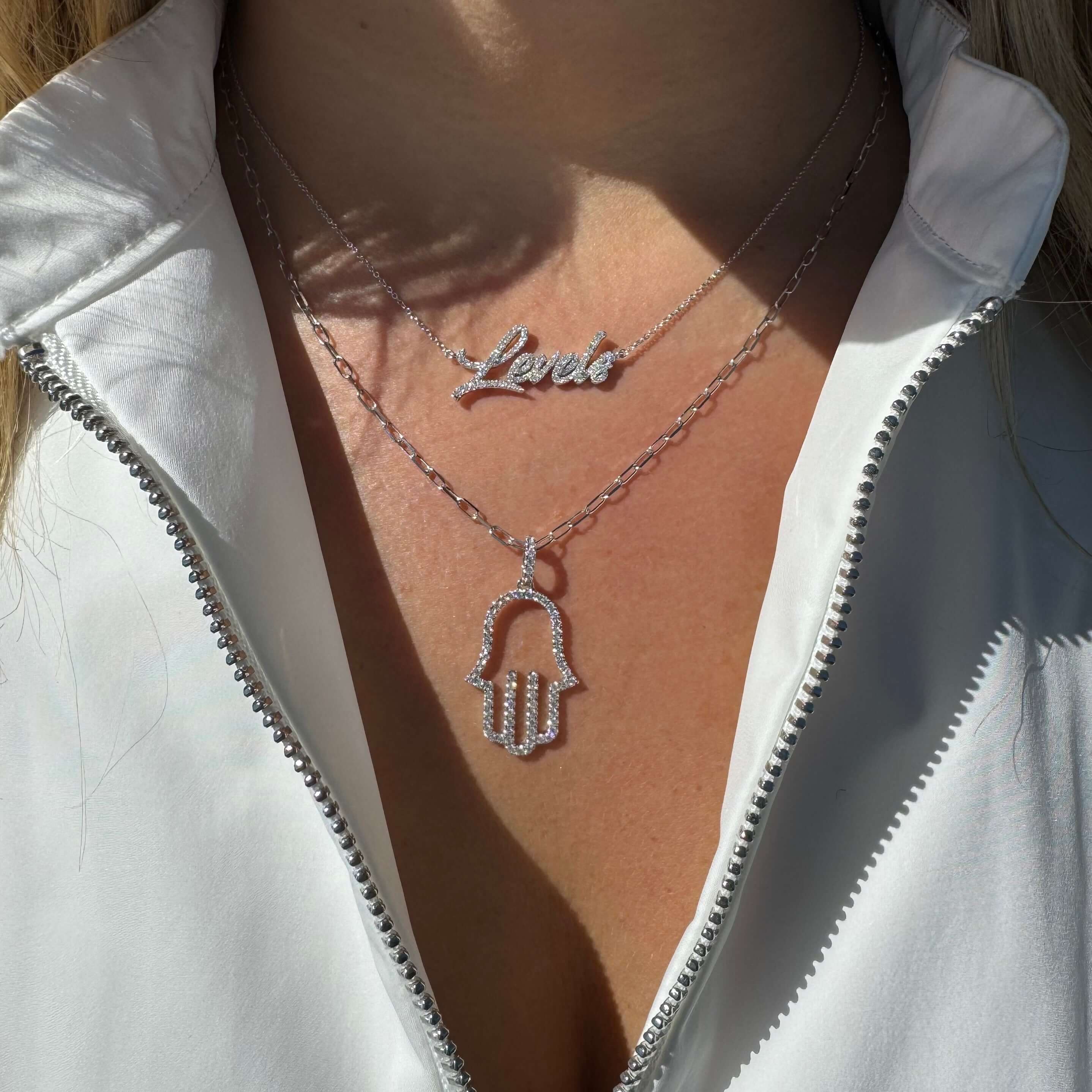 Layered silver necklaces featuring a 'Love' pendant and a hamsa symbol pendant for stylish elegance.