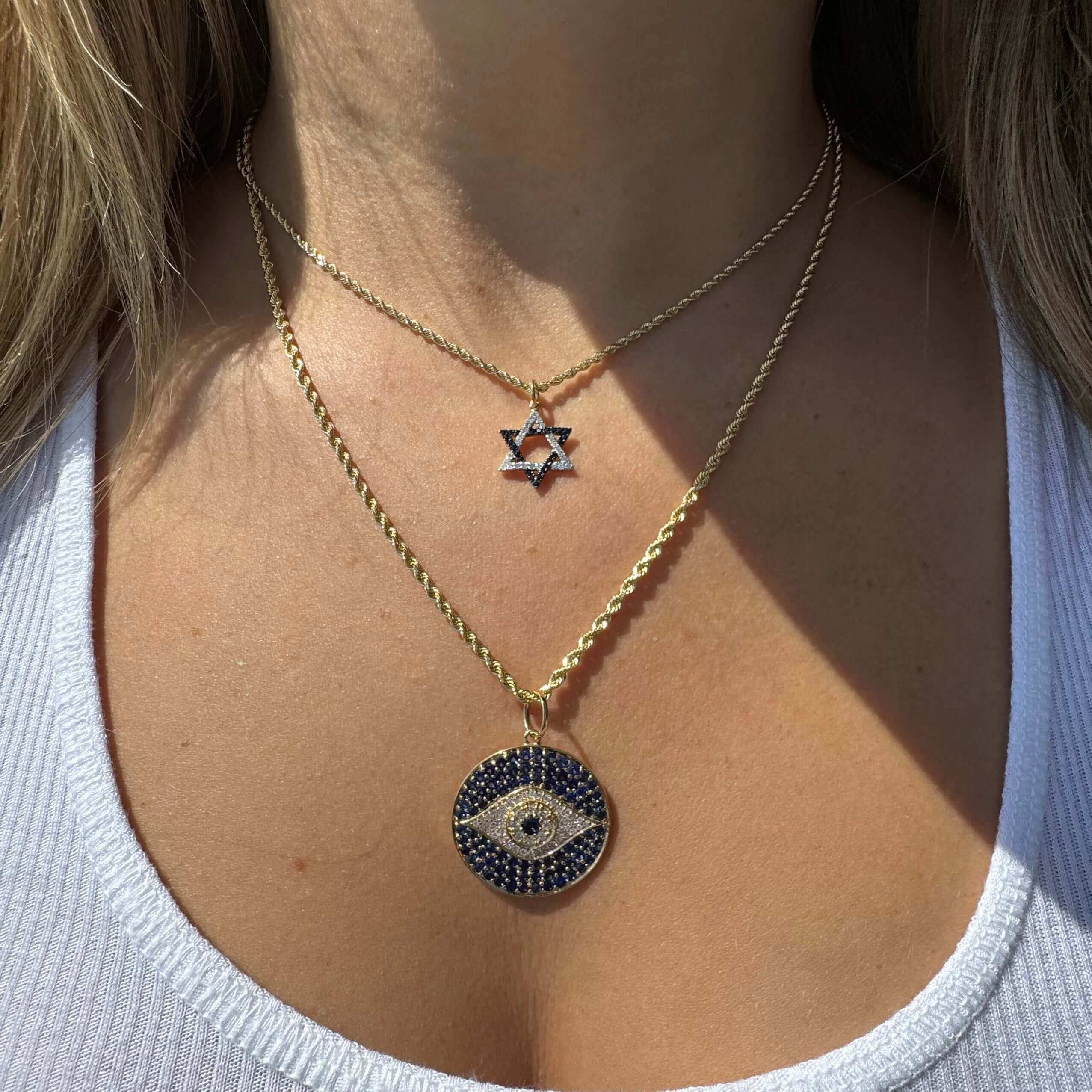 Stylish layered gold necklaces featuring a Star of David and an Evil Eye pendant against a white top, from our exquisite jewelry collection