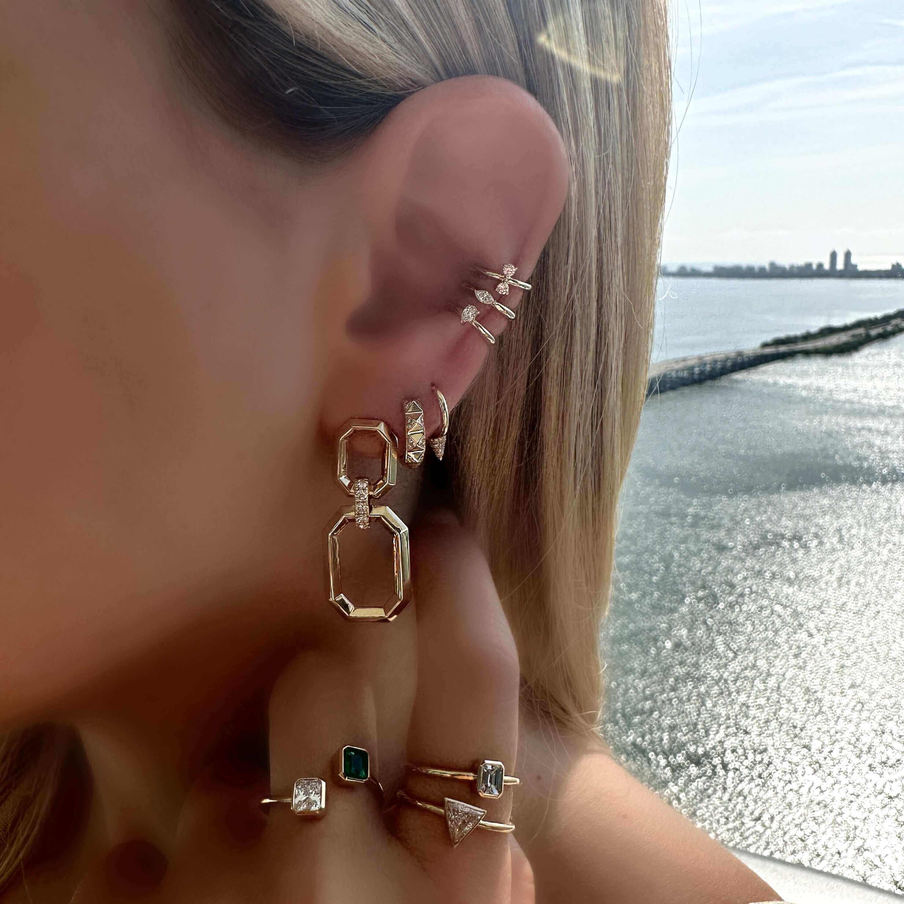 Woman wearing geometric earrings and stylish rings next to a serene water view