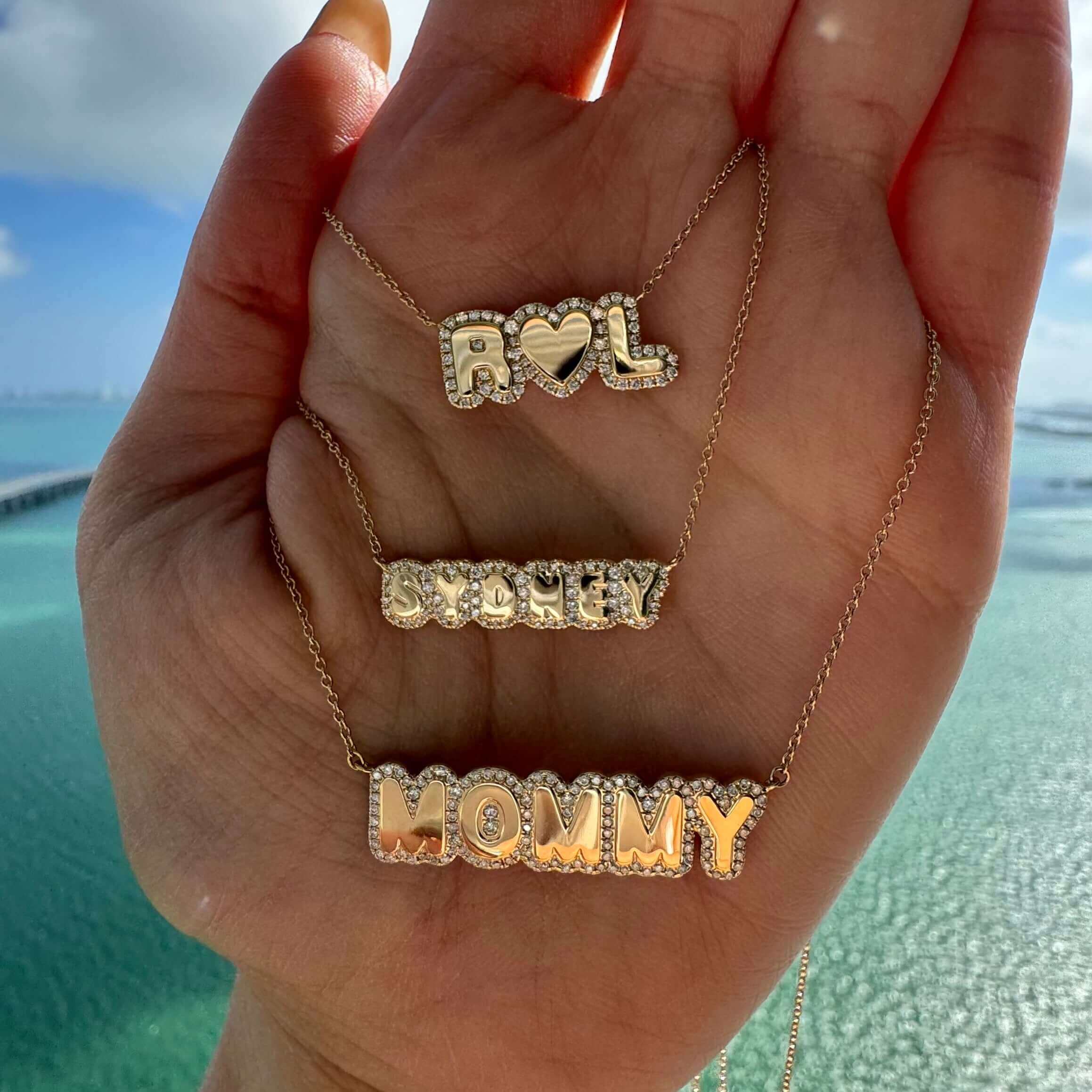 Personalized Diamond Cloud Nameplate Necklace displayed in hand with names 'ROL', 'SWEETY', and 'MOMMY' shining in sunlight.