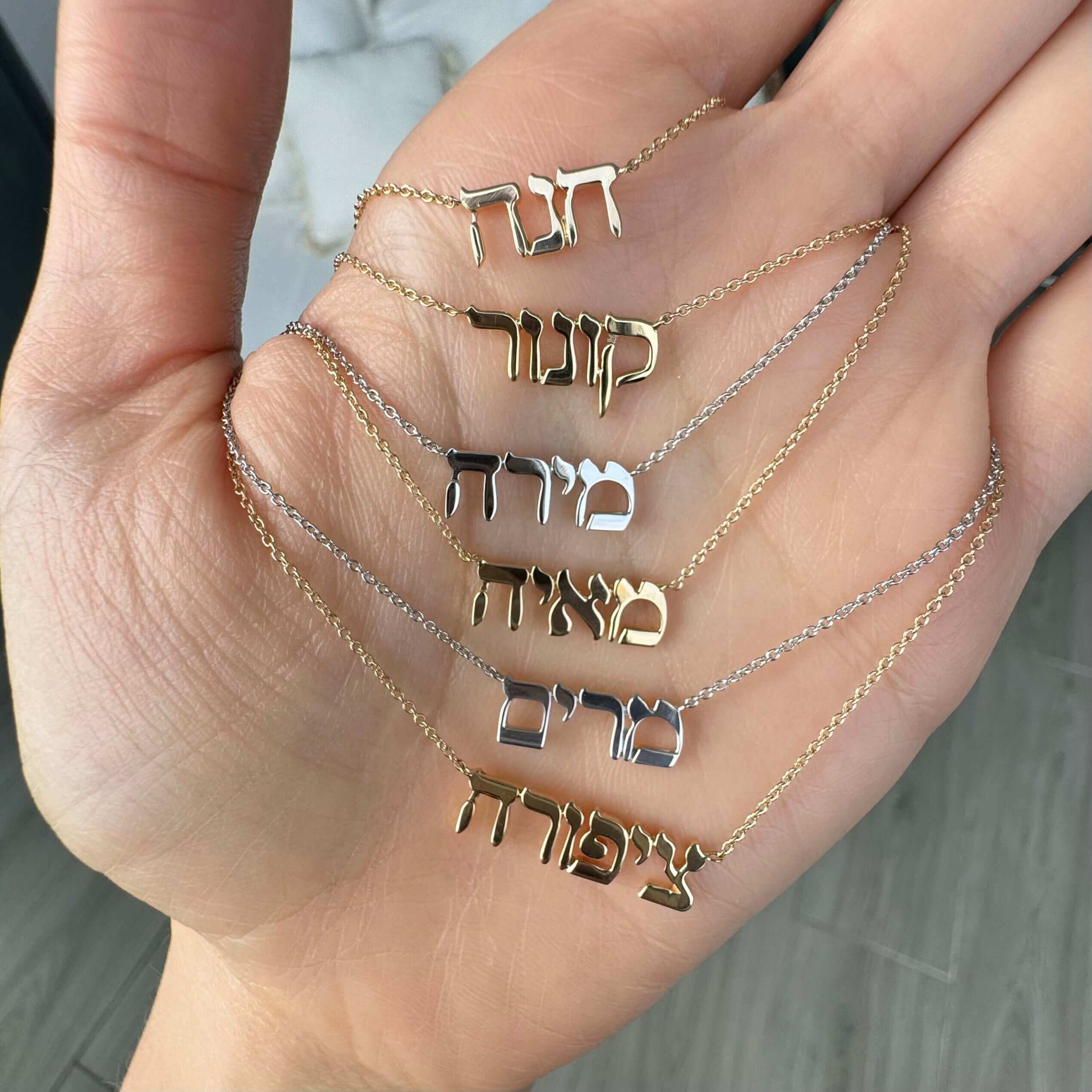 Hand holding Hebrew name necklaces in gold and silver from our jewelry brand