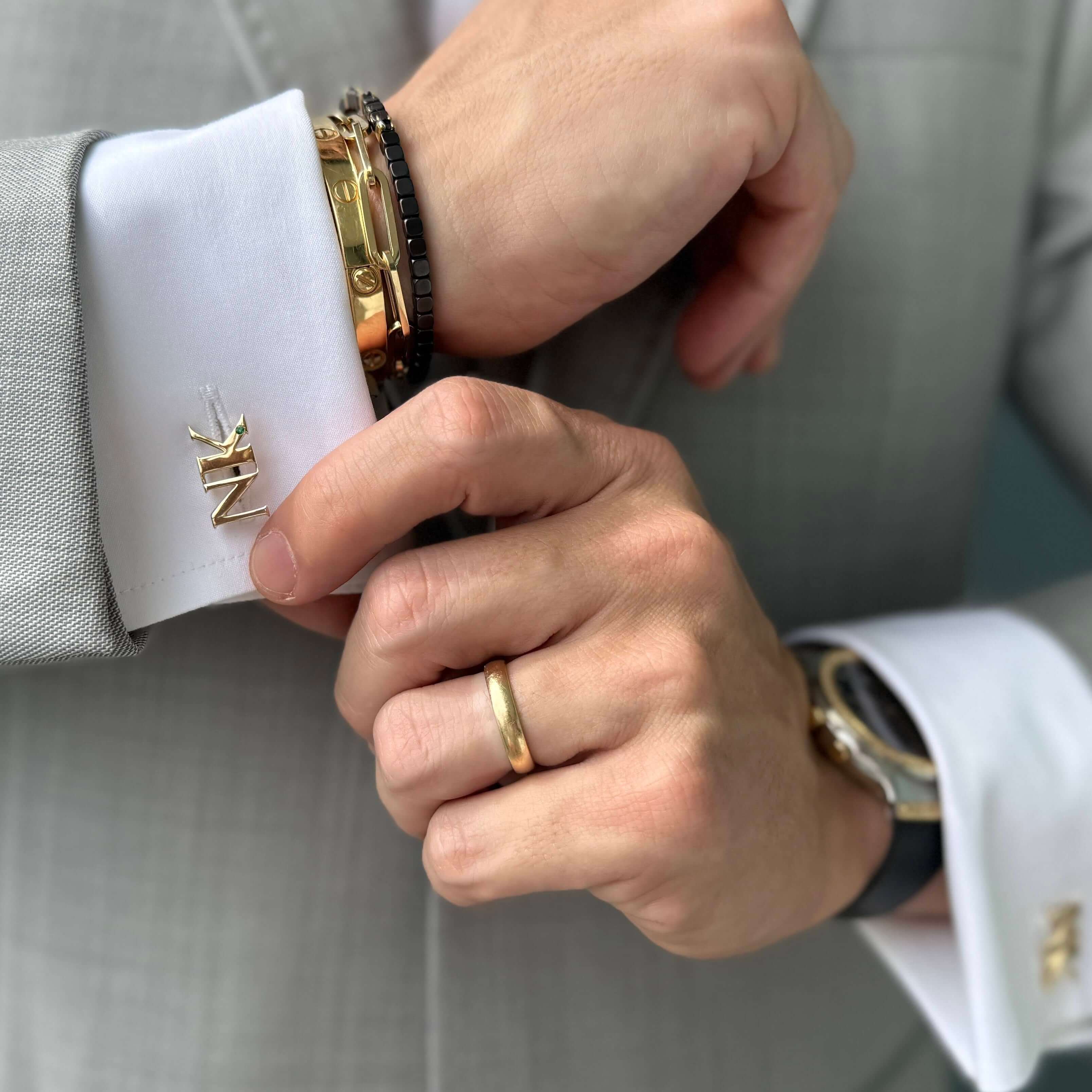 Close-up of a well-dressed man adjusting his cufflinks and wearing stylish bracelets and a wedding ring.