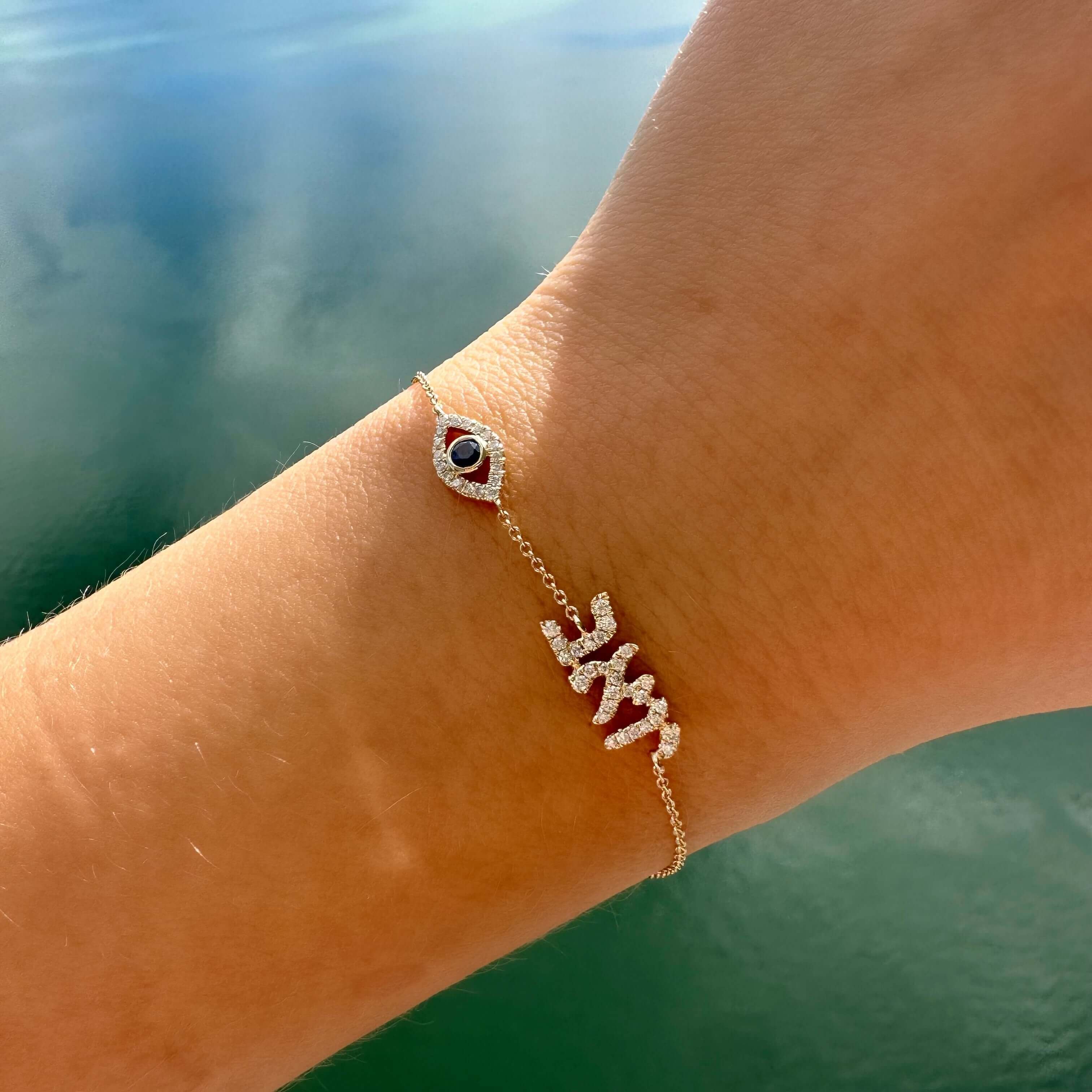 Personalized Motif Hebrew Diamond Nameplate Bracelet featuring diamond and sapphire evil eye on wrist.