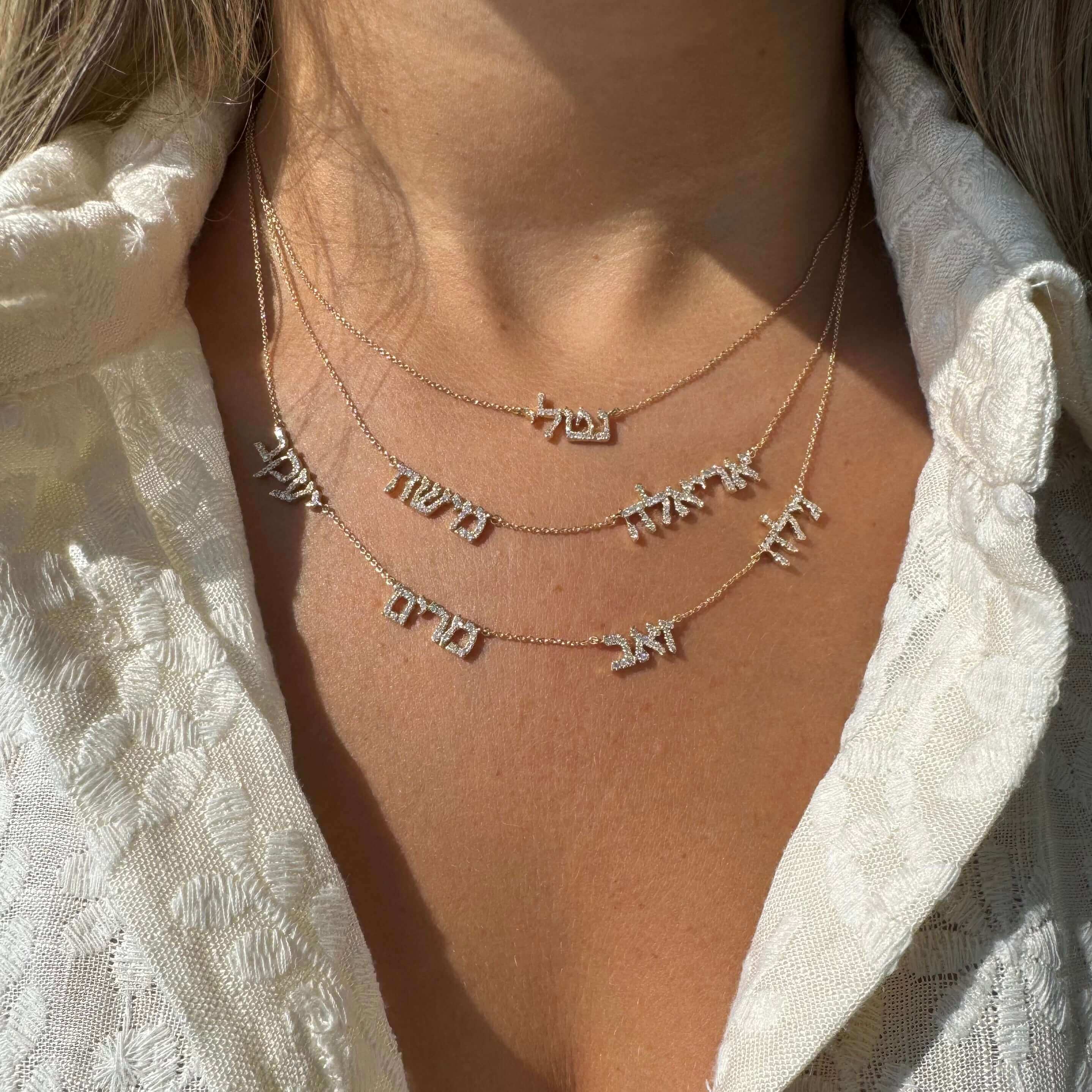 Woman wearing layered gold necklaces with Hebrew name pendants from our jewelry collection