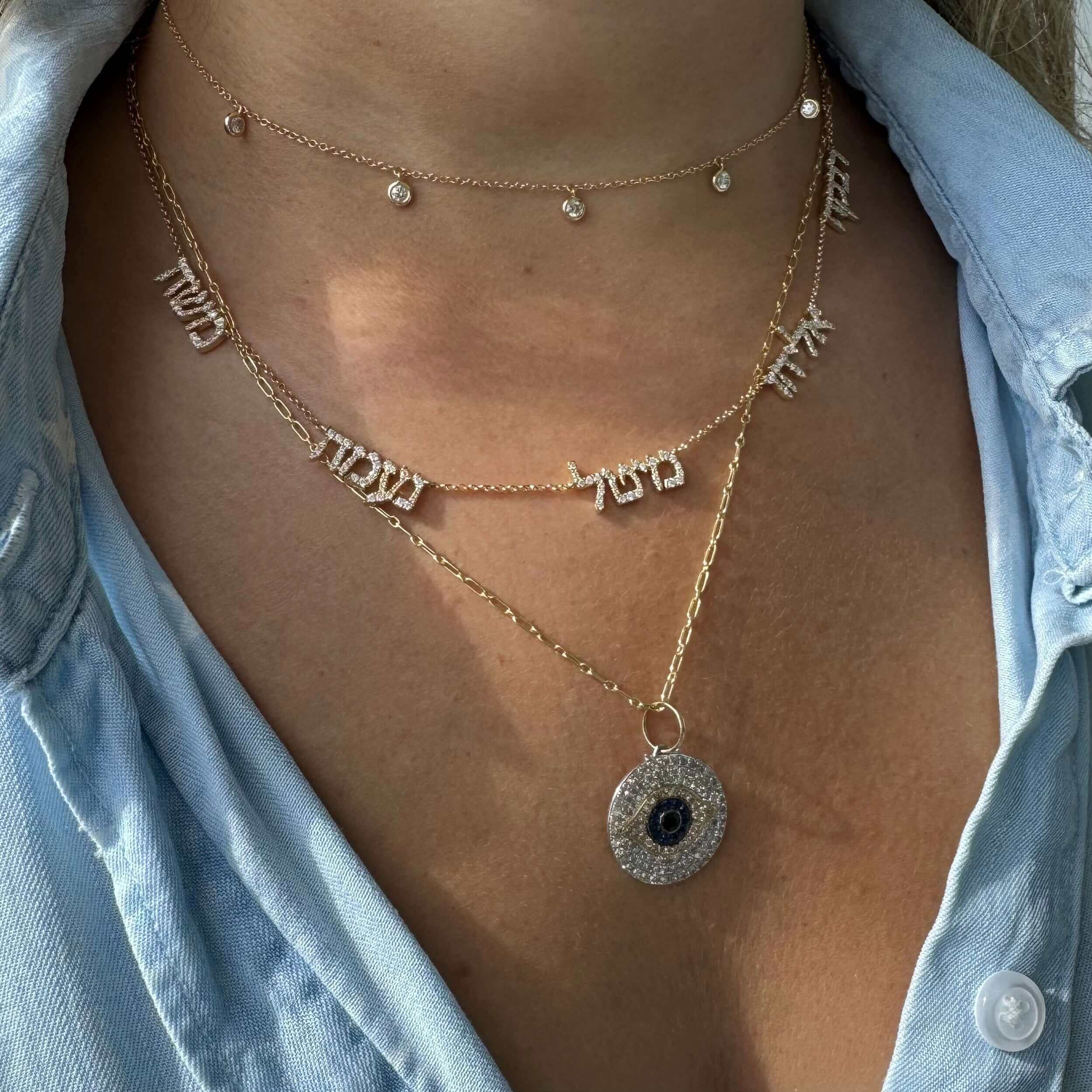 Woman wearing layered necklaces with Hebrew letters and a sparkling pendant from our jewelry brand.