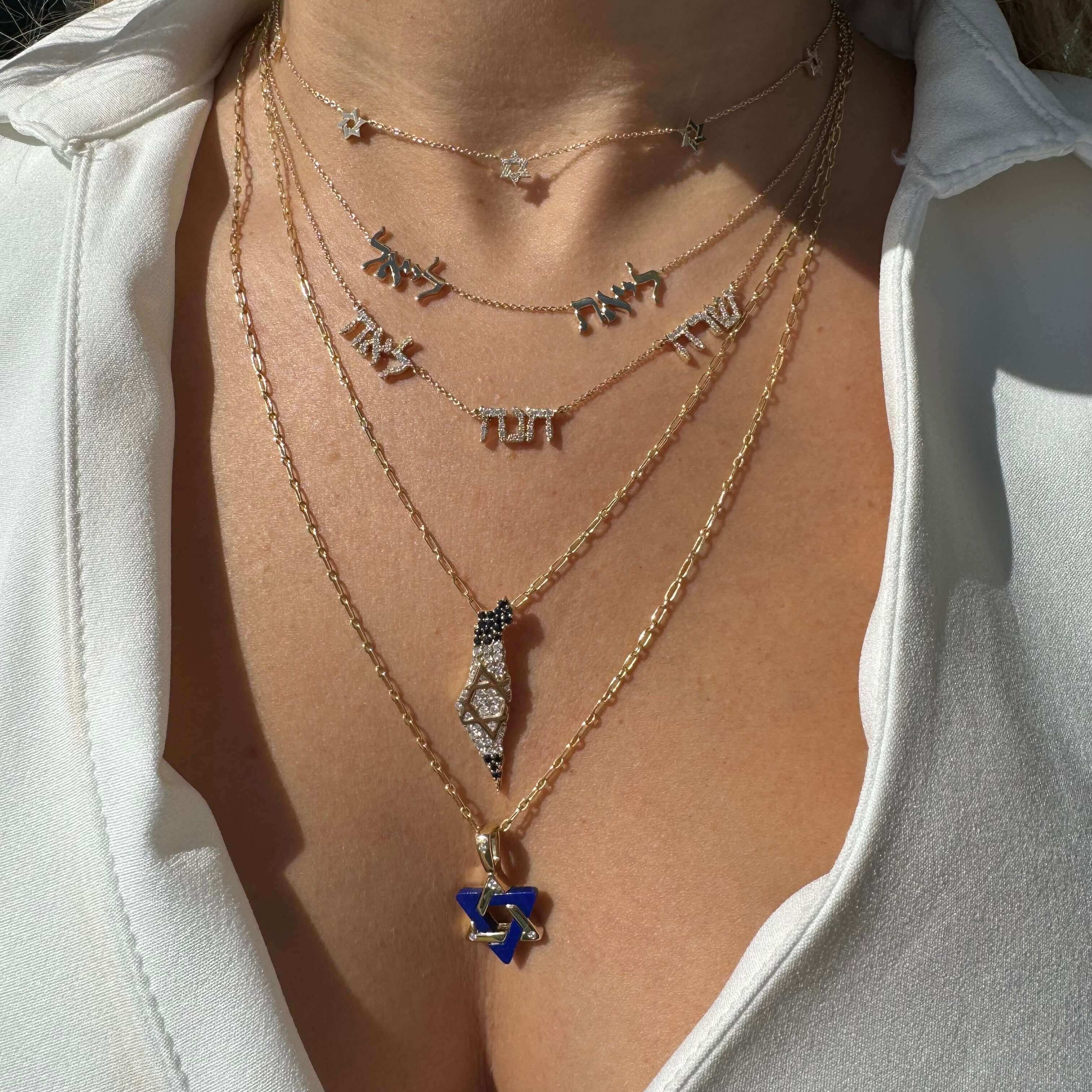 Woman wearing layered gold necklaces with Hebrew letters and a blue gemstone pendant, showcasing our elegant jewelry collection.