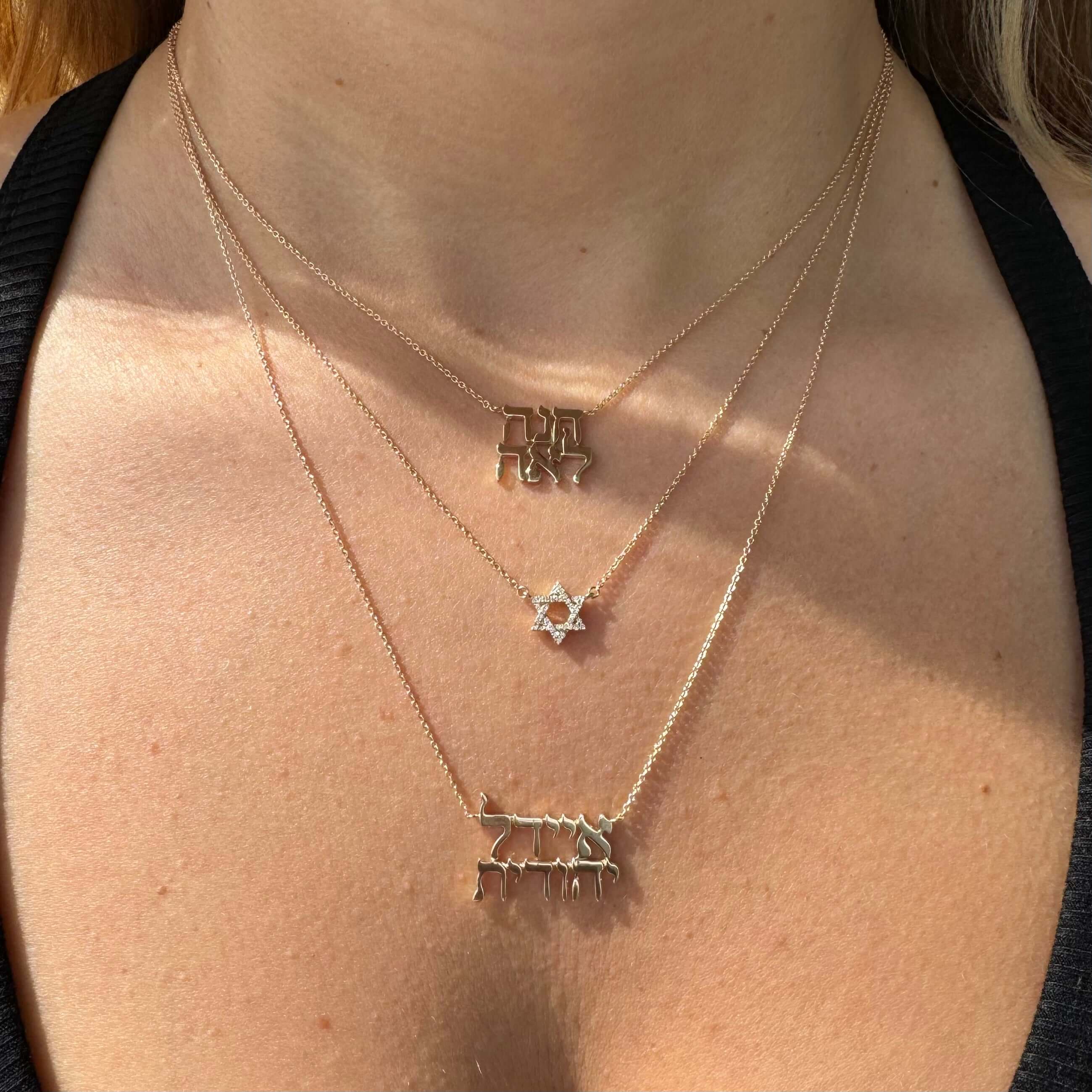 14K gold personalized stacked Hebrew nameplate necklaces displayed on a woman's neck, showcasing unique designs and heritage.