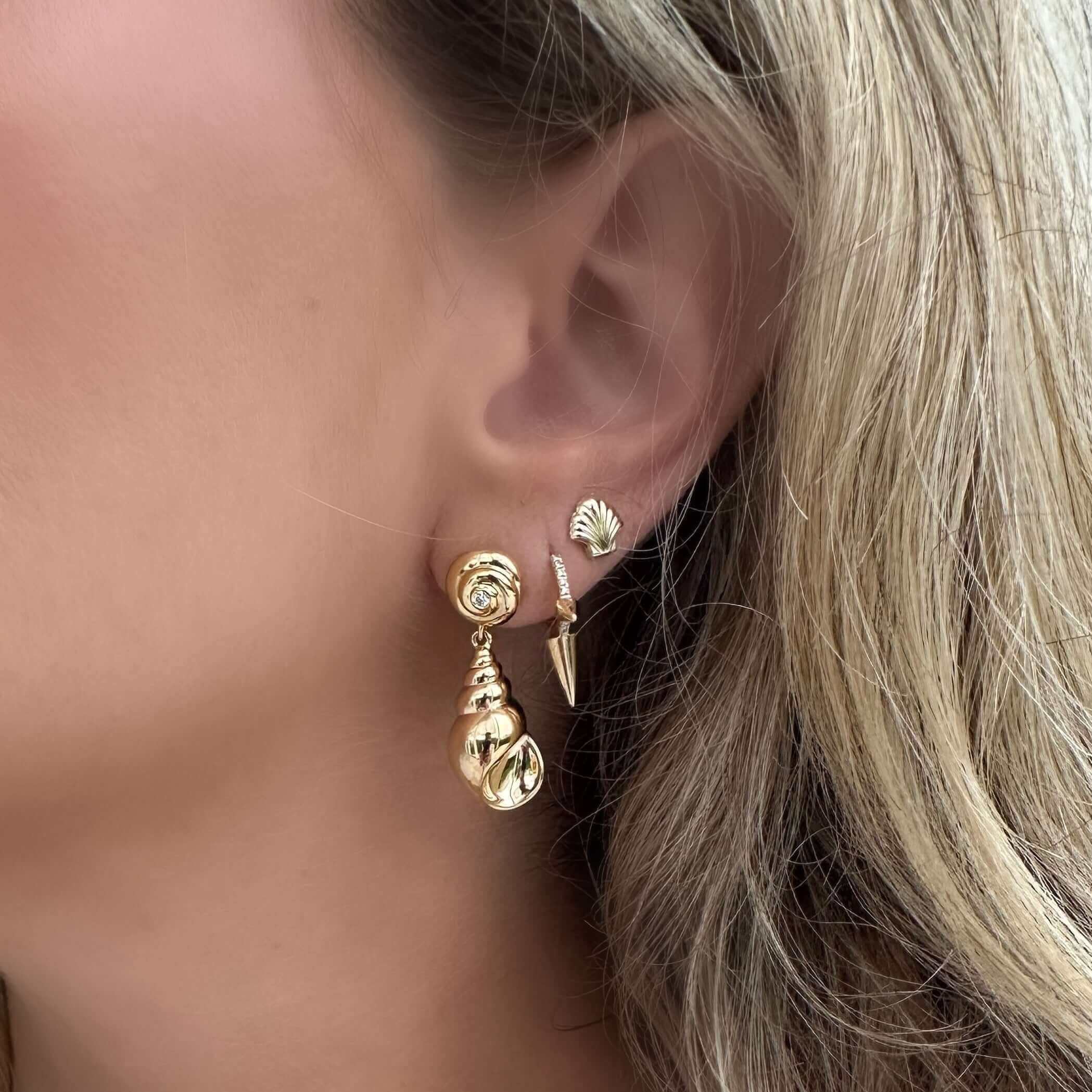 A close-up of a model wearing Petite Scallop Shell Button Gold Earrings paired with other elegant gold earrings.