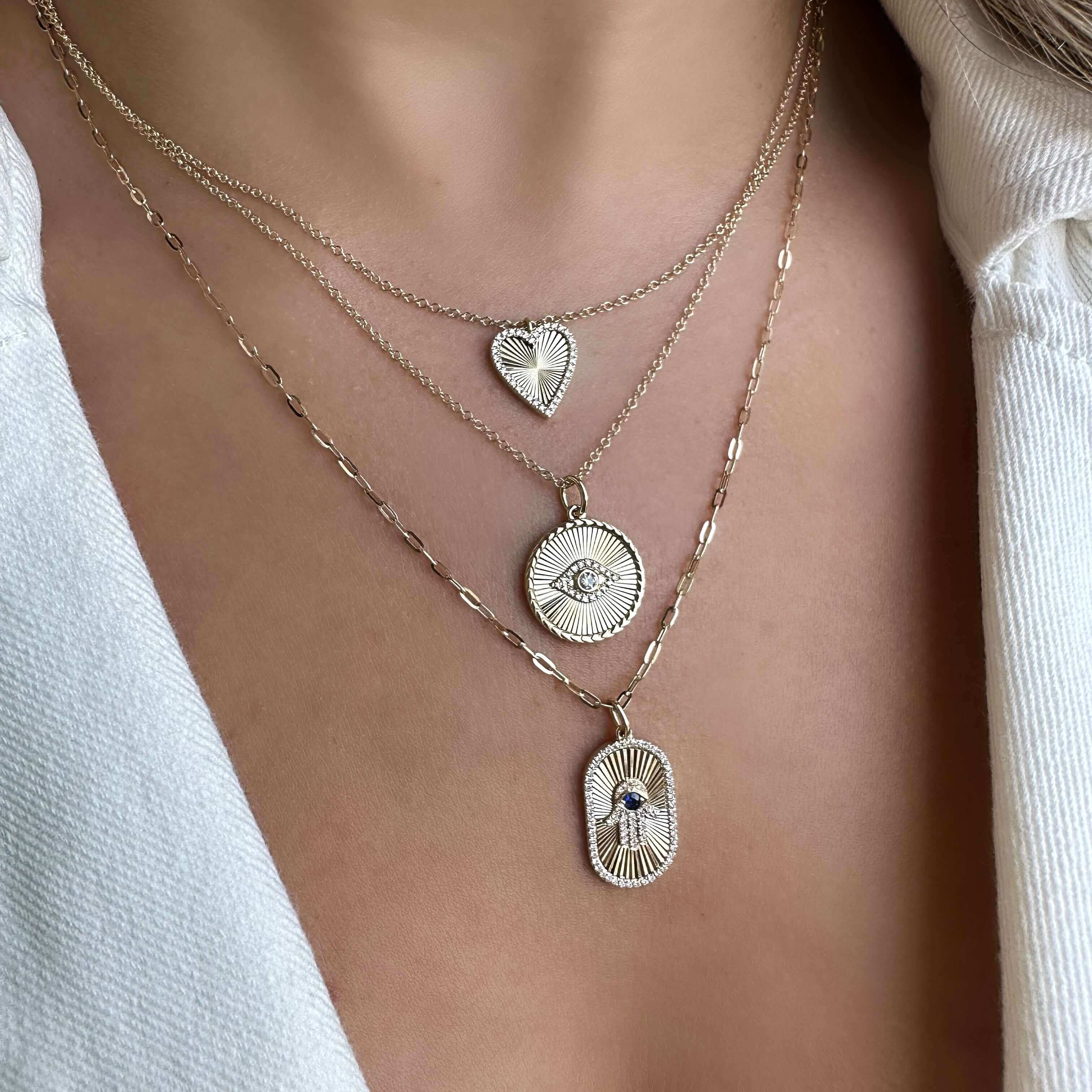 Layered gold necklaces with pendants, including a heart and eye, from our exclusive jewelry collection.