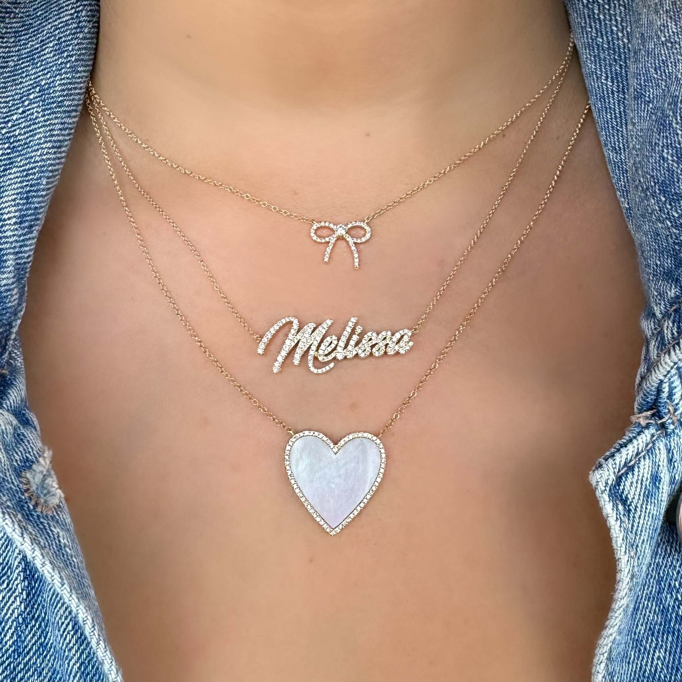 Layered necklace set featuring a bow tie charm, name 'Melissa', and a heart pendant on a denim background.
