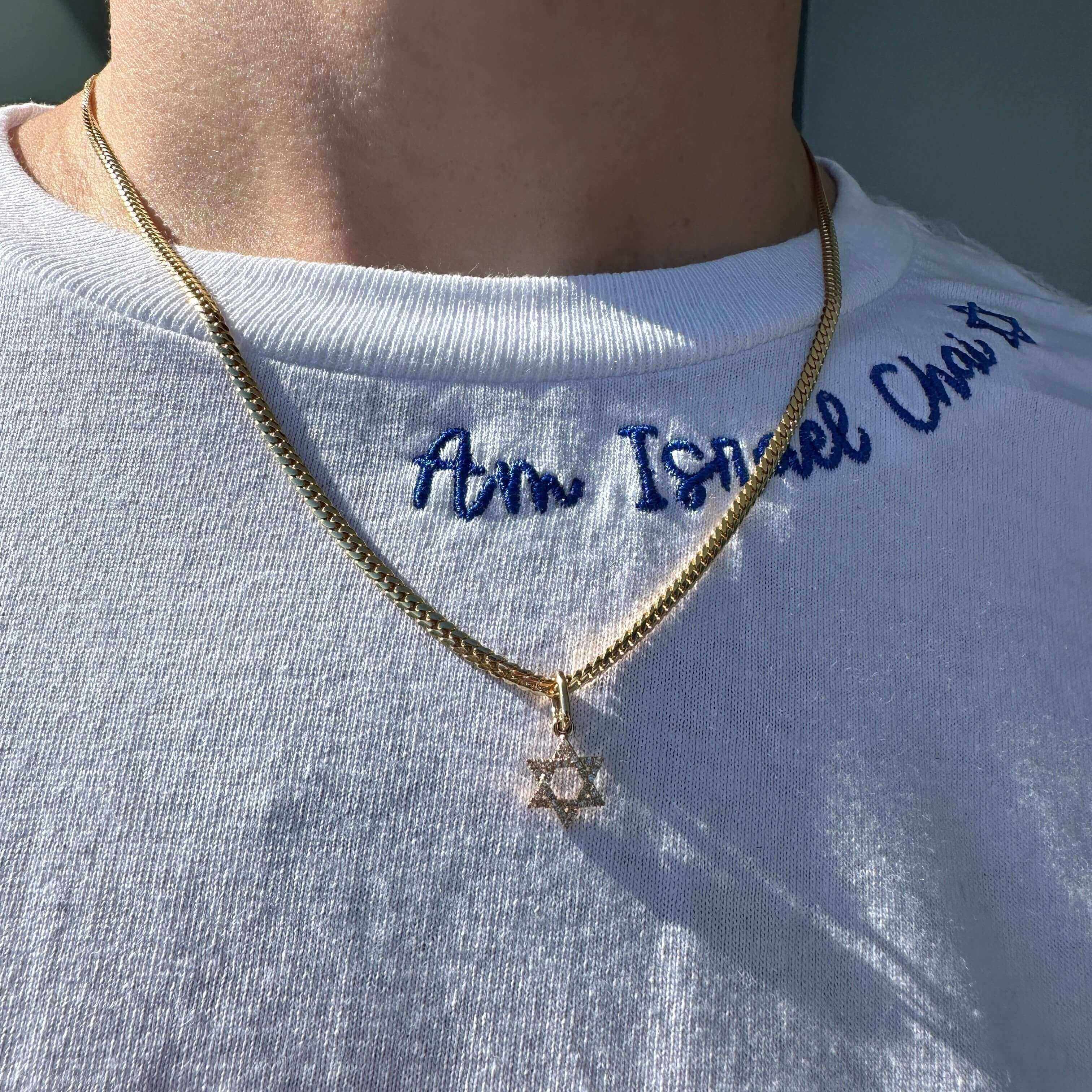 Stylish gold Star of David necklace on a white shirt with blue embroidery.