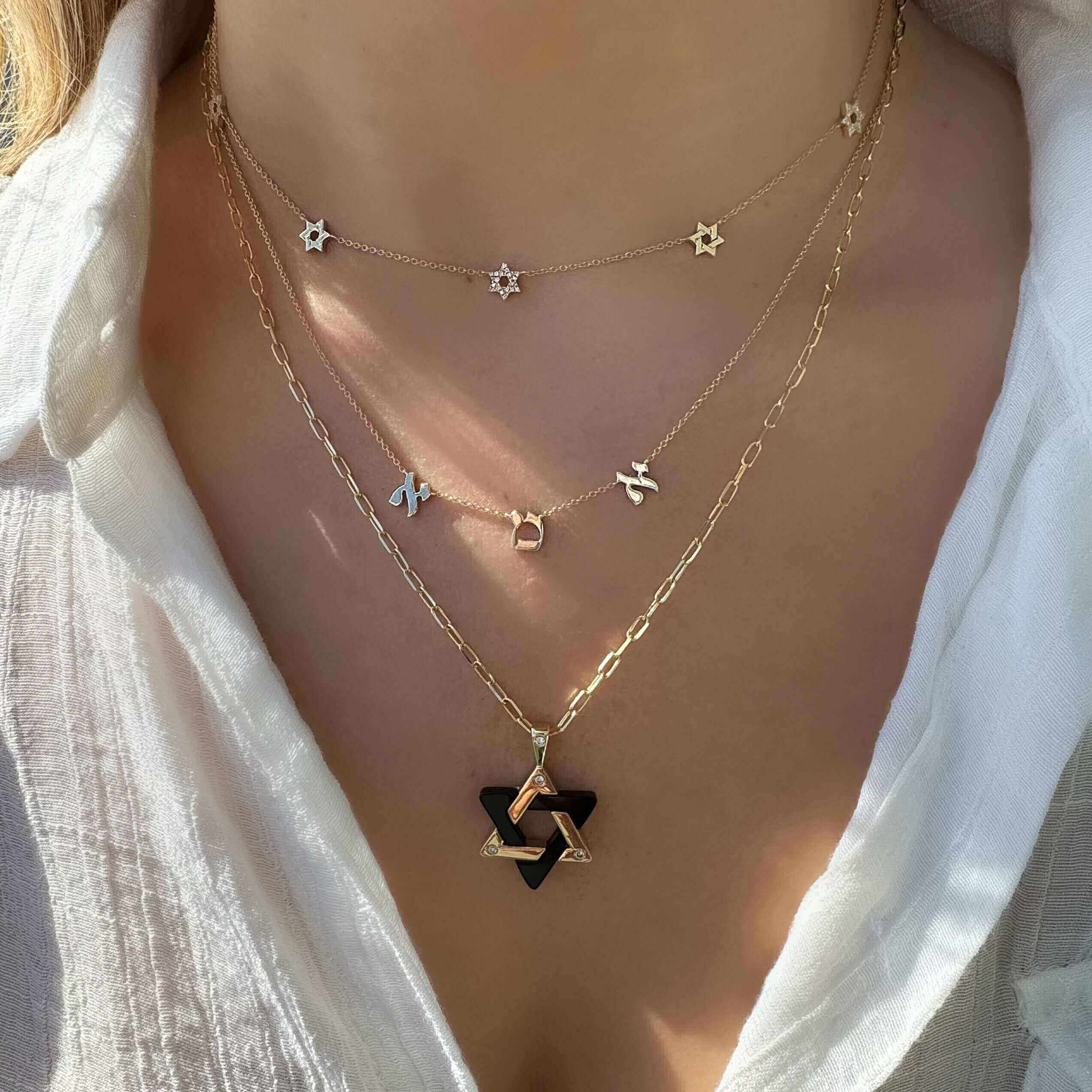 Woman wearing layered 14K gold necklaces, featuring Stars of David and hexagram pendants.