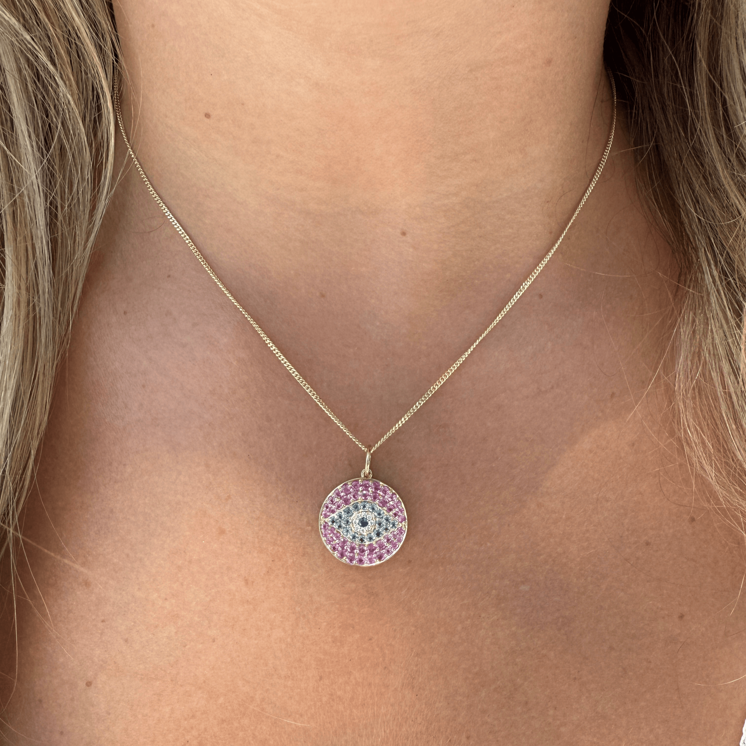 14K gold evil eye necklace charm with topaz and sapphire, worn on a model's neck for a stylish protective talisman.